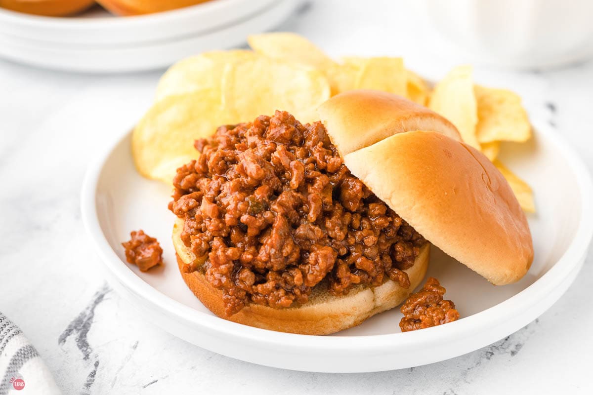 white plate with a ground beef sandwich with potato chips