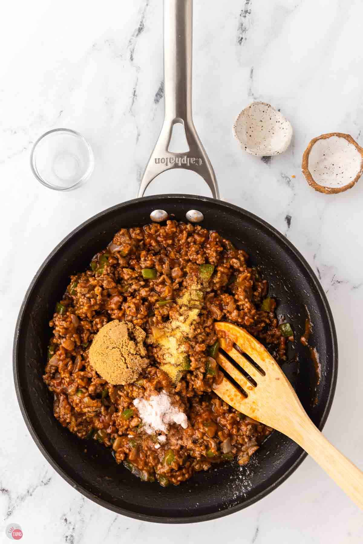 skillet with cooked ground beef and spices being stirred with a wood spoon