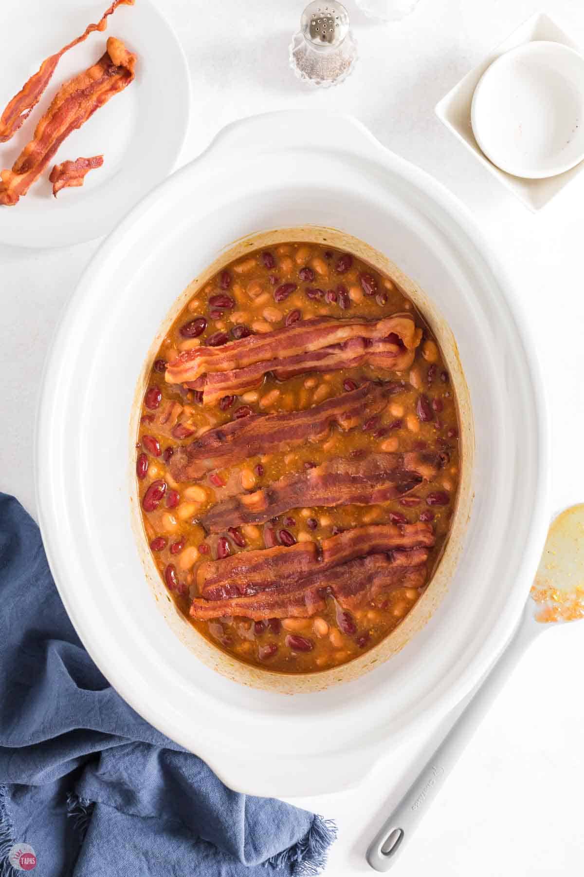 baked beans and bacon in a white crock pot