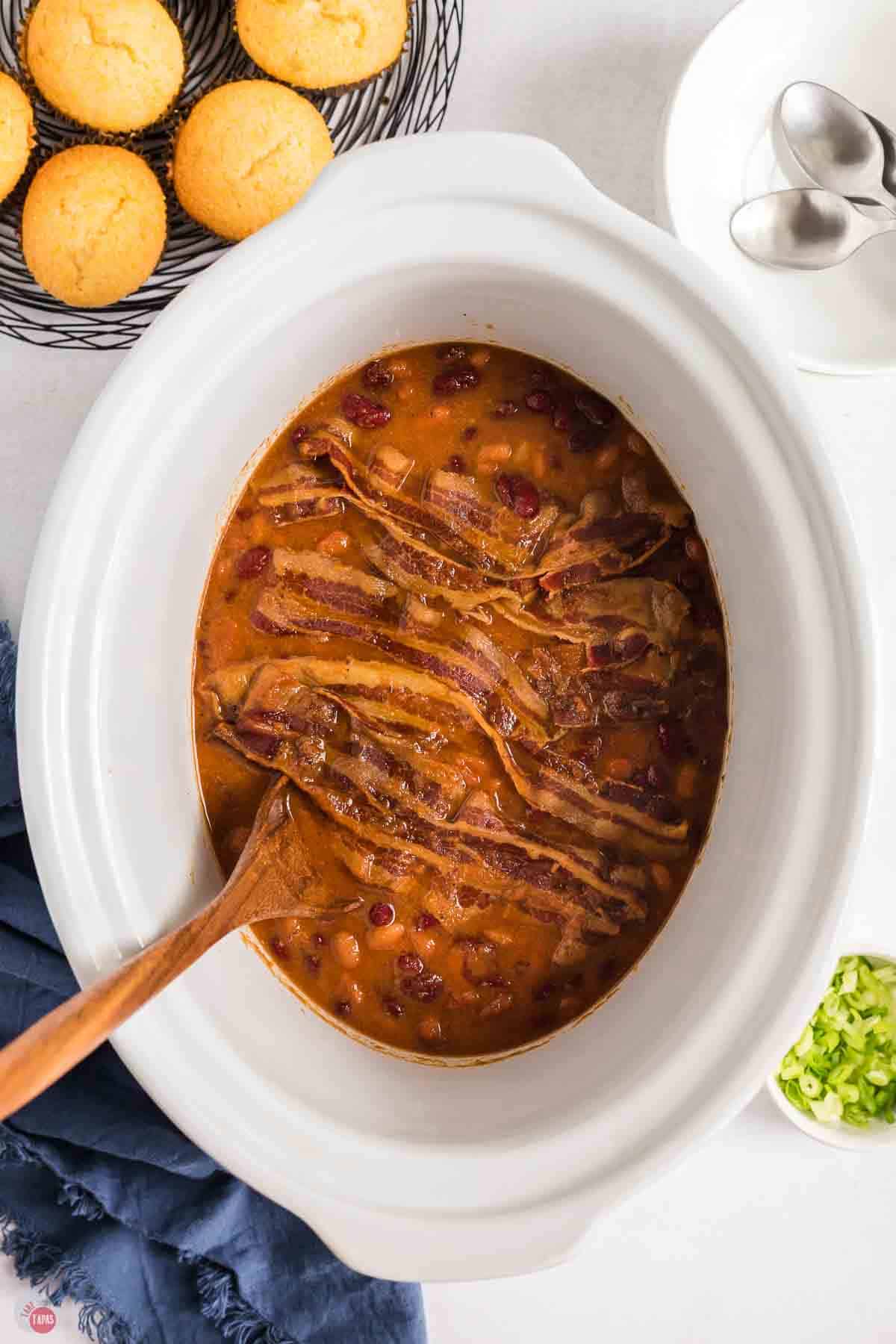white crock pot with beans and strips of bacon