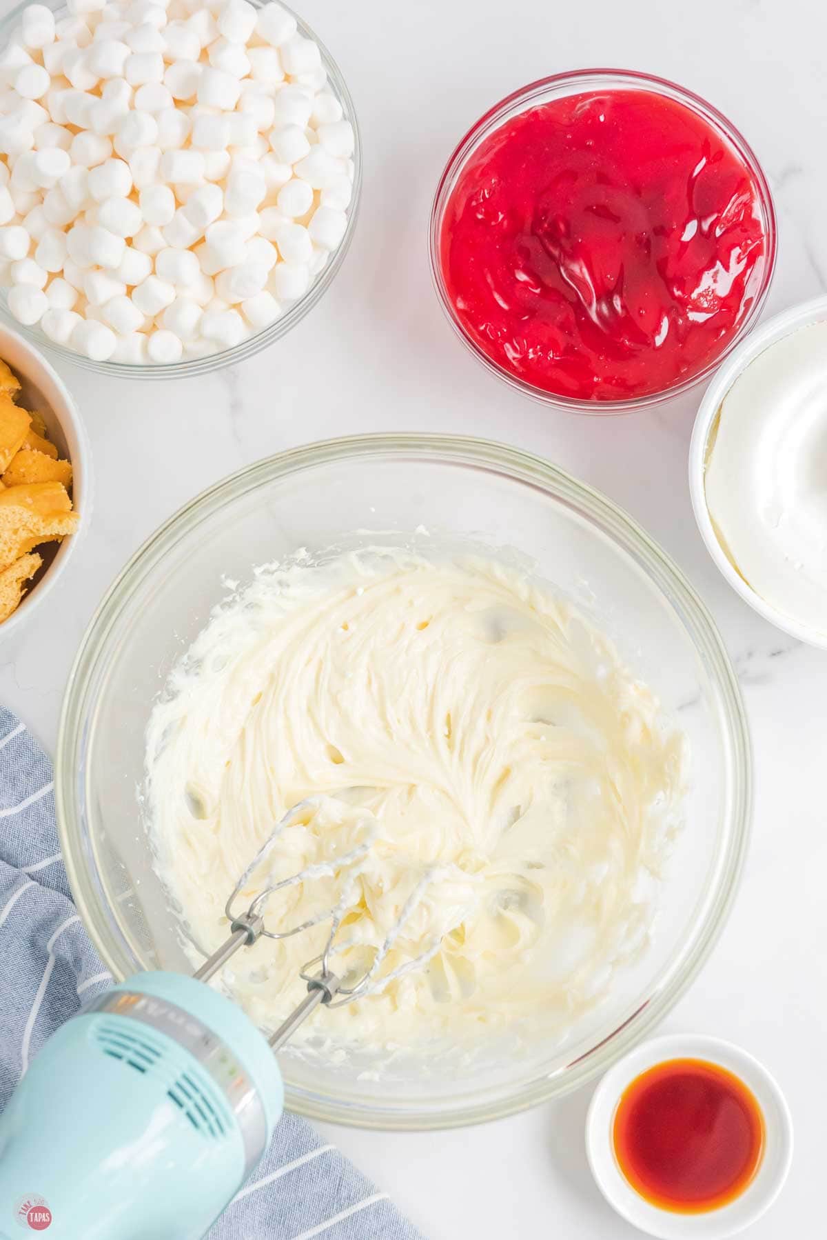 mixer combining sugar and cream cheese in a clear bowl