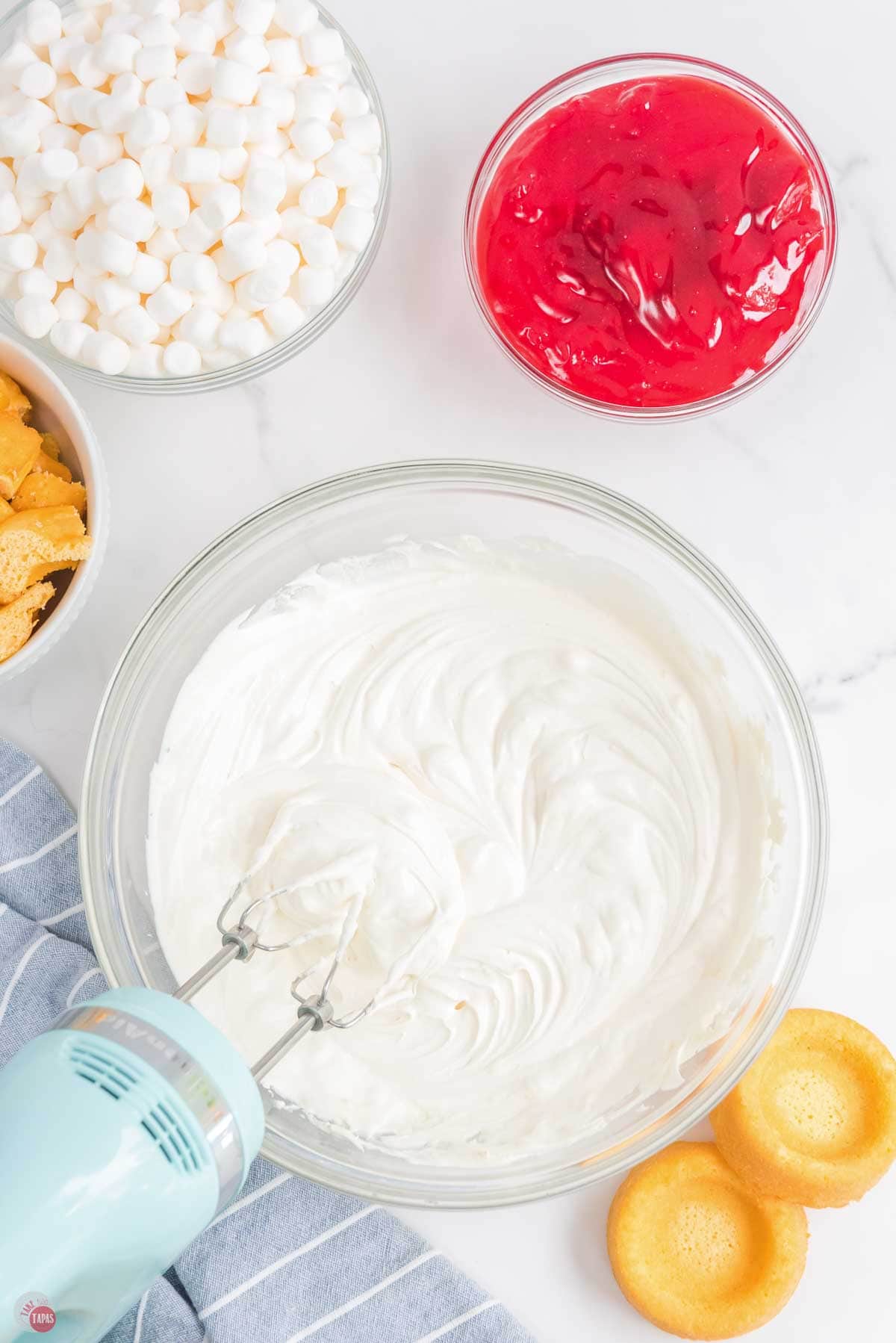 cream cheese icing in a clear bowl with a blue hand mixer