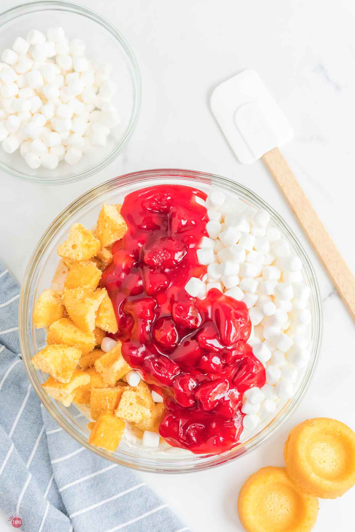clear bowl with cake cubes, pie filling, and marshmallows in it