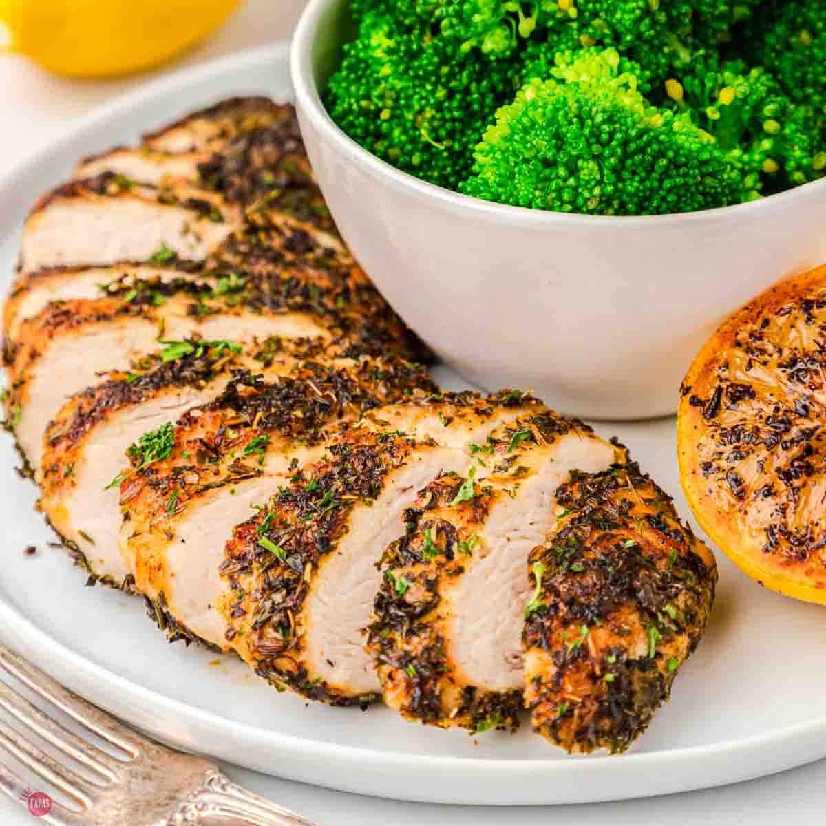 slices of herb chicken on a plate with broccoli