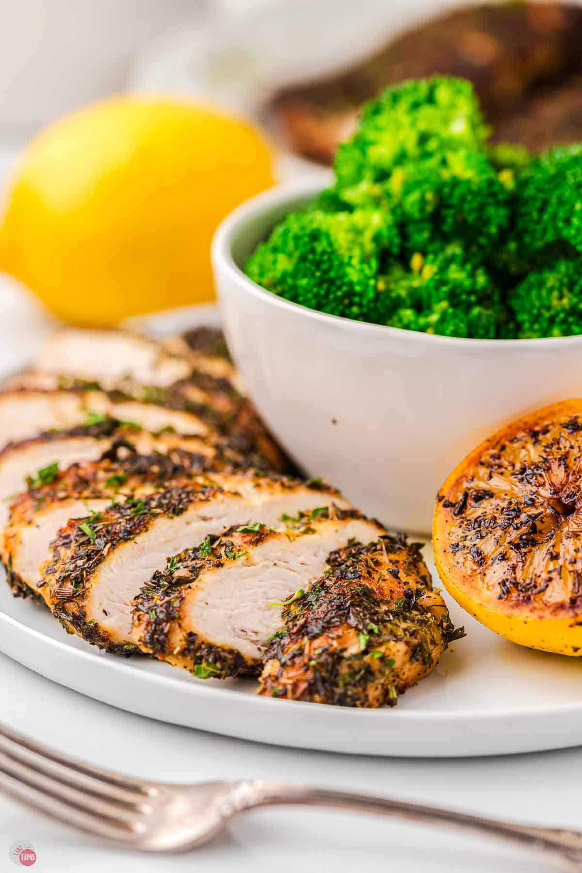 sliced chicken on a plate with a bowl of broccoli