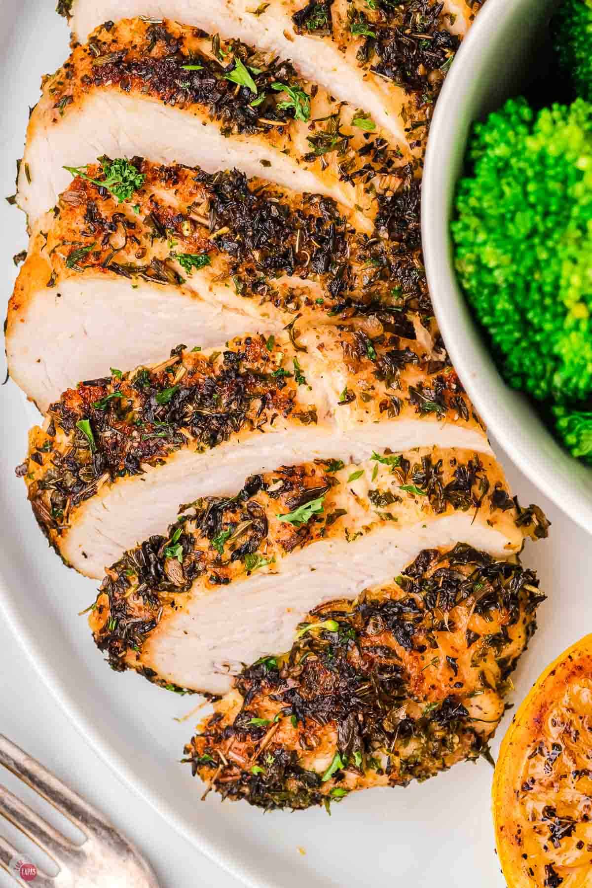 herb chicken breast sliced on a plate with a bowl of broccoli
