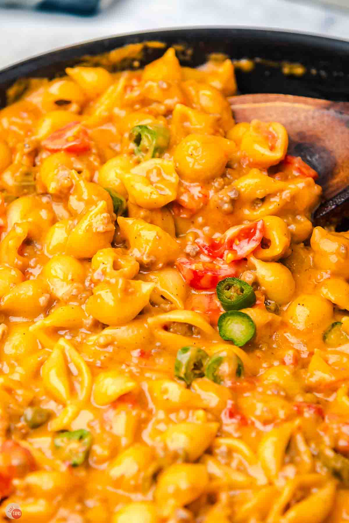 close up of cheesy pasta and ground beef with a wood spoon