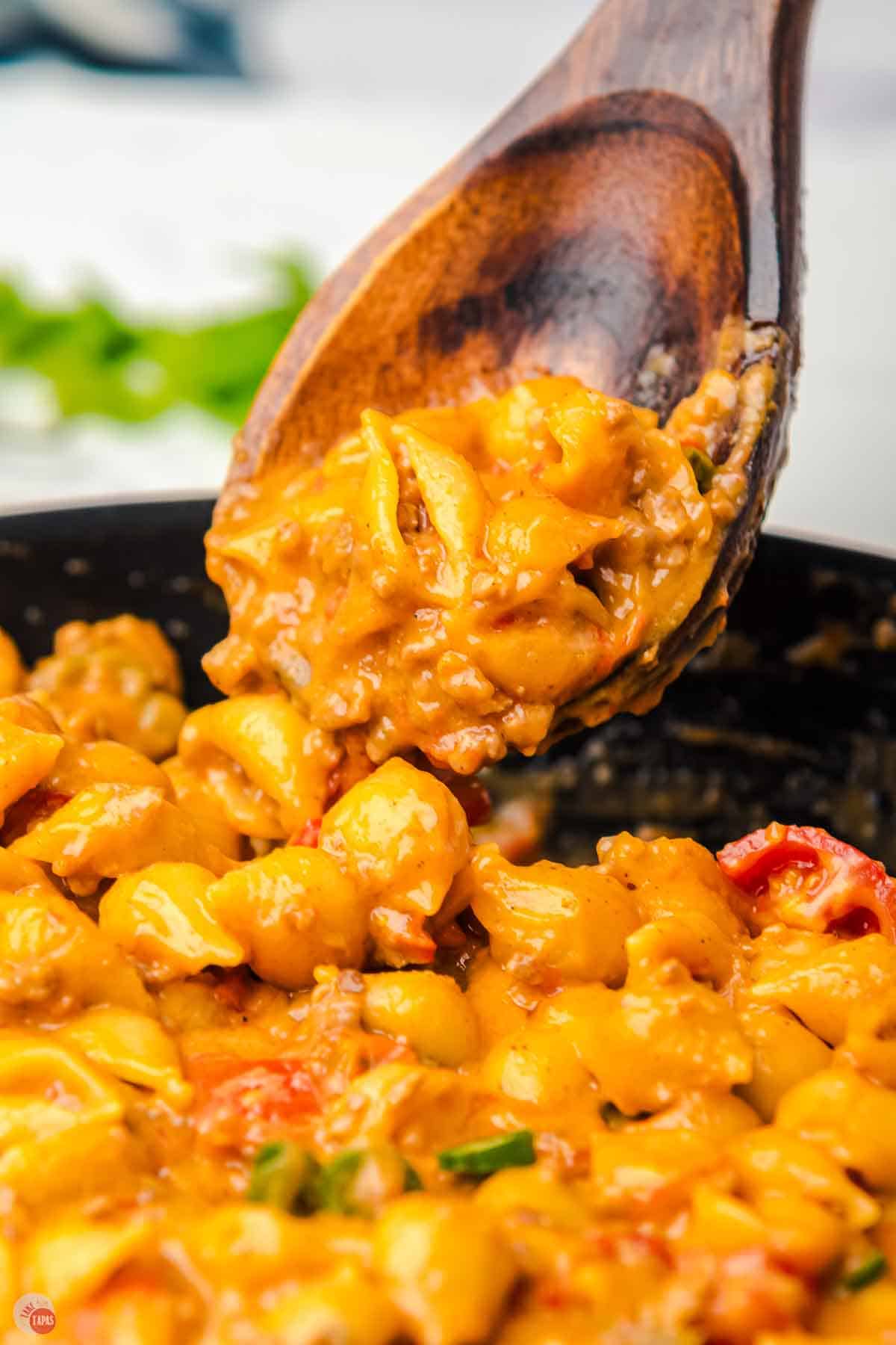 wood spoon with pasta and sauce on it right next to a skillet
