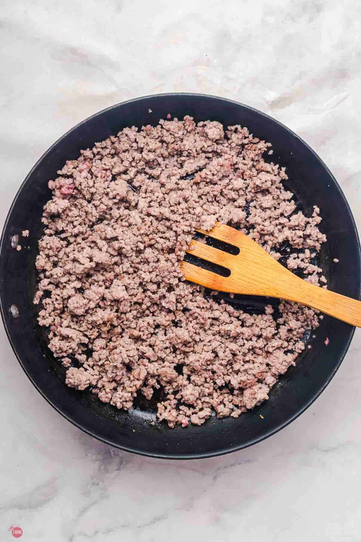 cooked ground beef in a black skillet with a wood fork