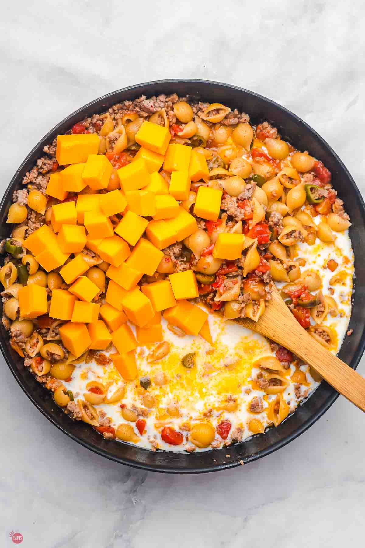 black skillet with cooked pasta shells, ground beef, milk, and cubes of cheese