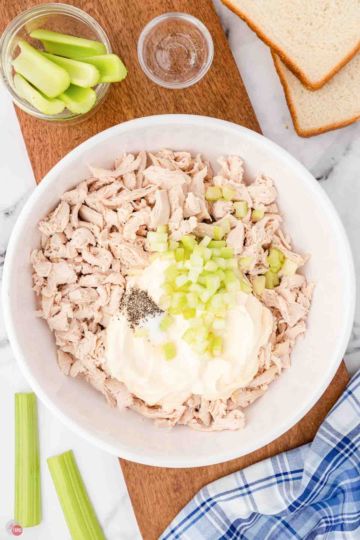 shredded chicken in a bowl topped with mayo and celery
