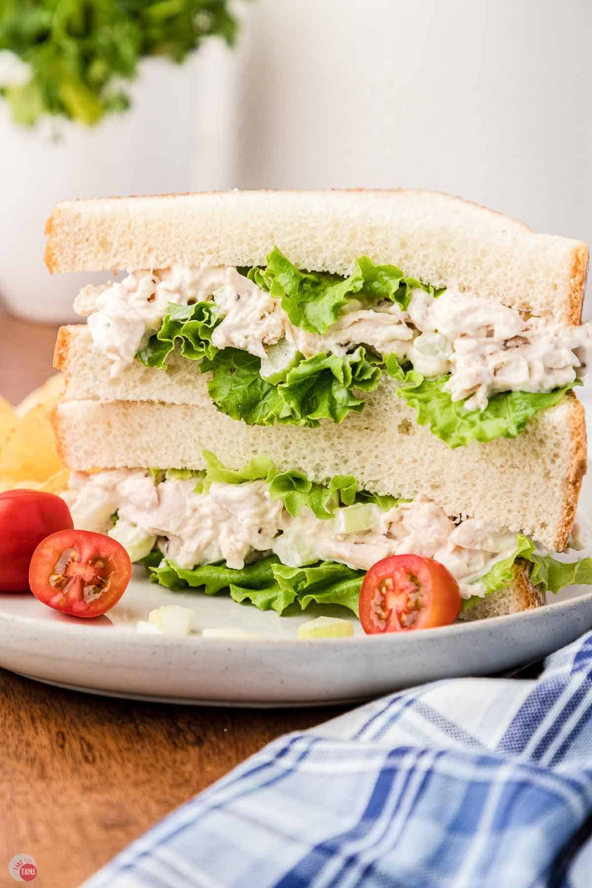 white plate with a cut chicken salad sandwich next to a blue napkin