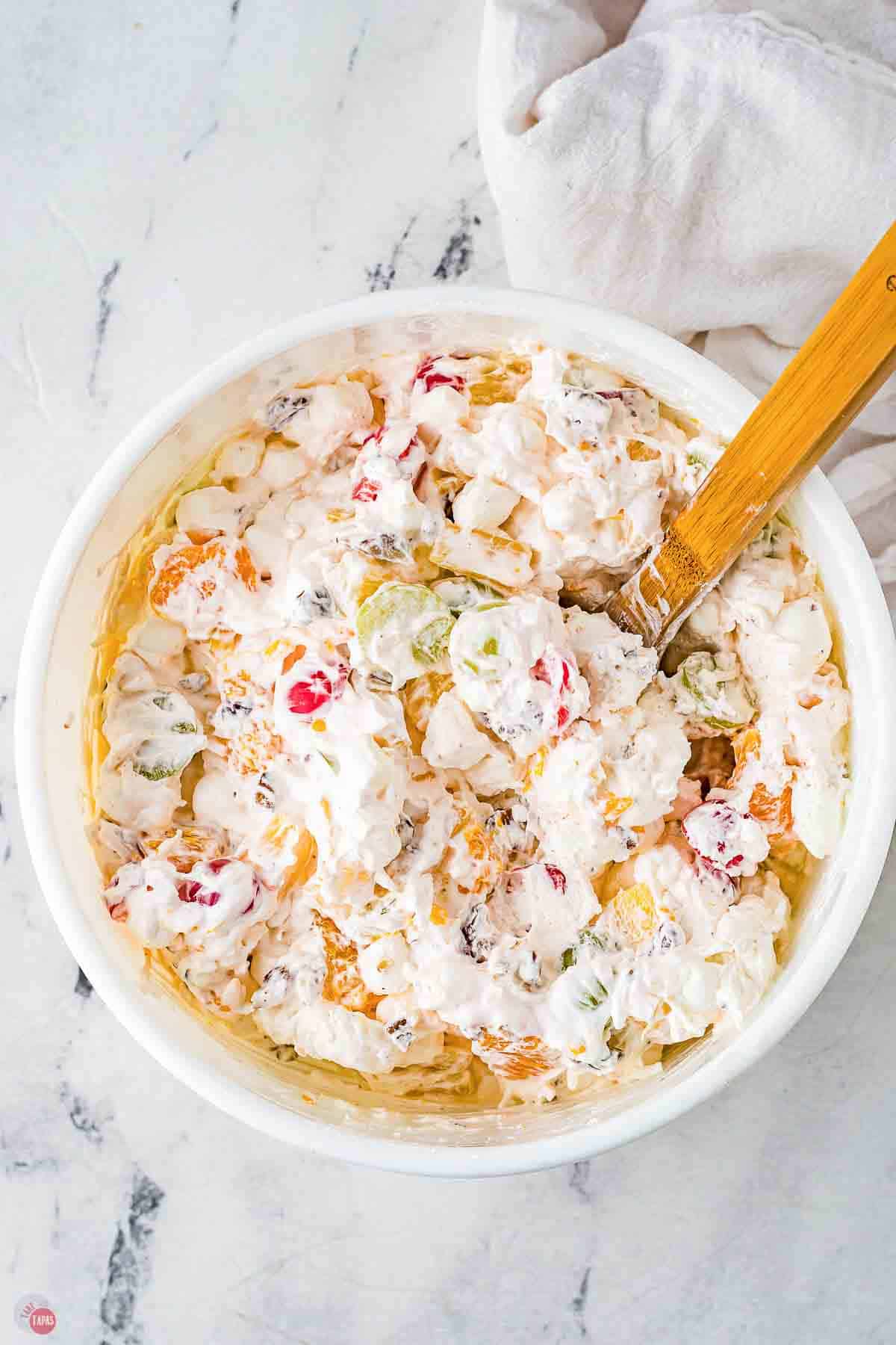 white bowl of ambrosia salad with a wood spoon