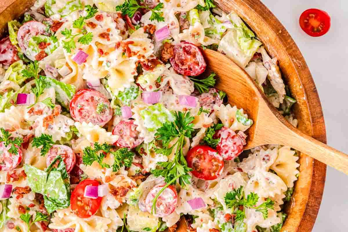 close up of pasta salad in a bowl with a wood spoon