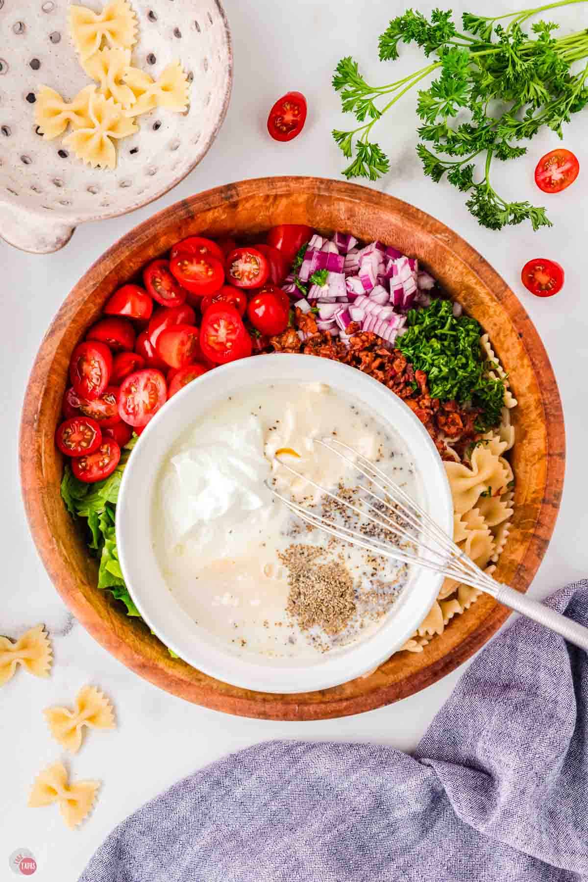 bowl of chopped vegetables with a small bowl inside it with dressing ingredients being whisked together