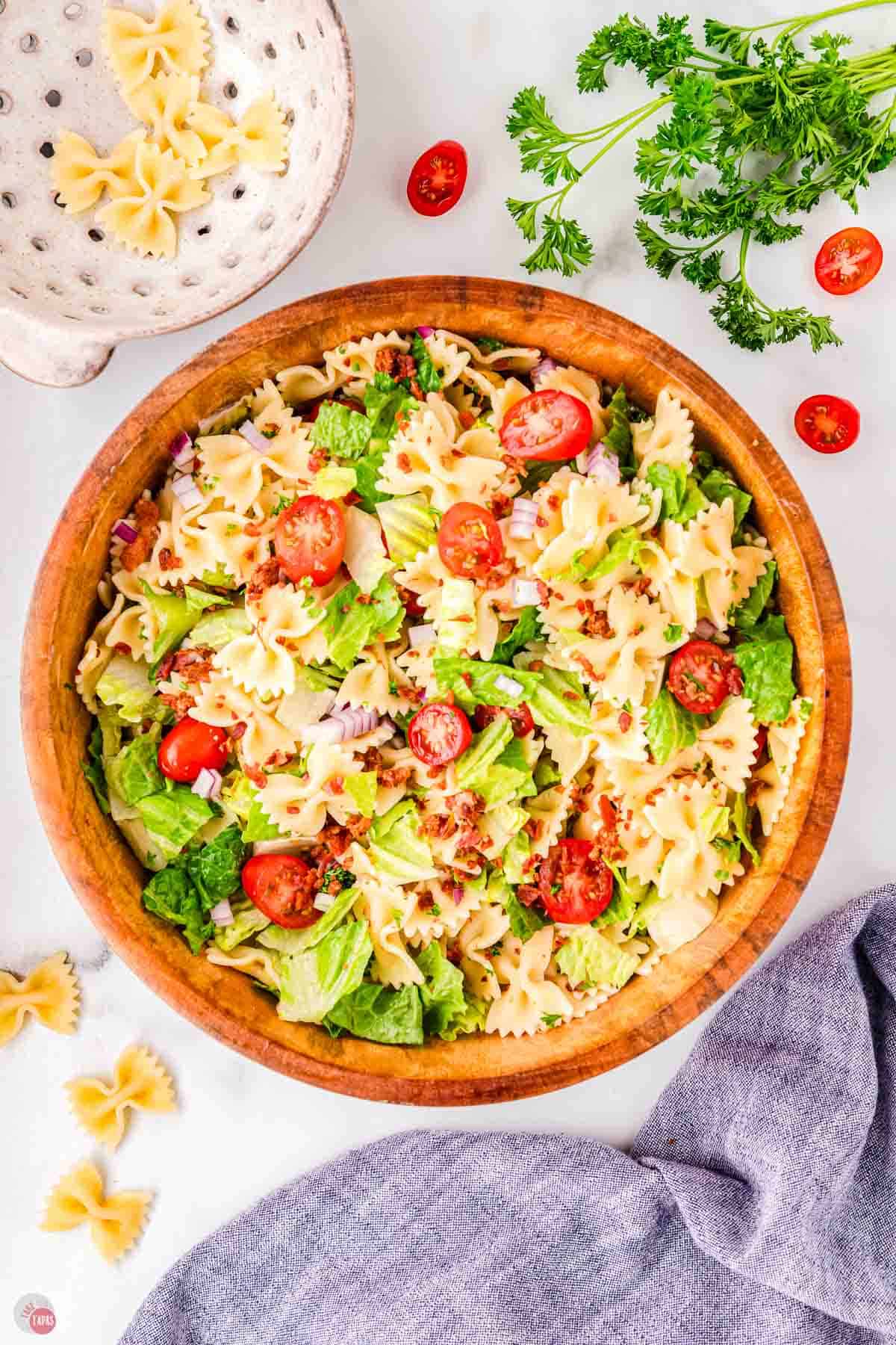 bowl of cooked pasta mixed with lettuce, tomatoes, and crispy bacon