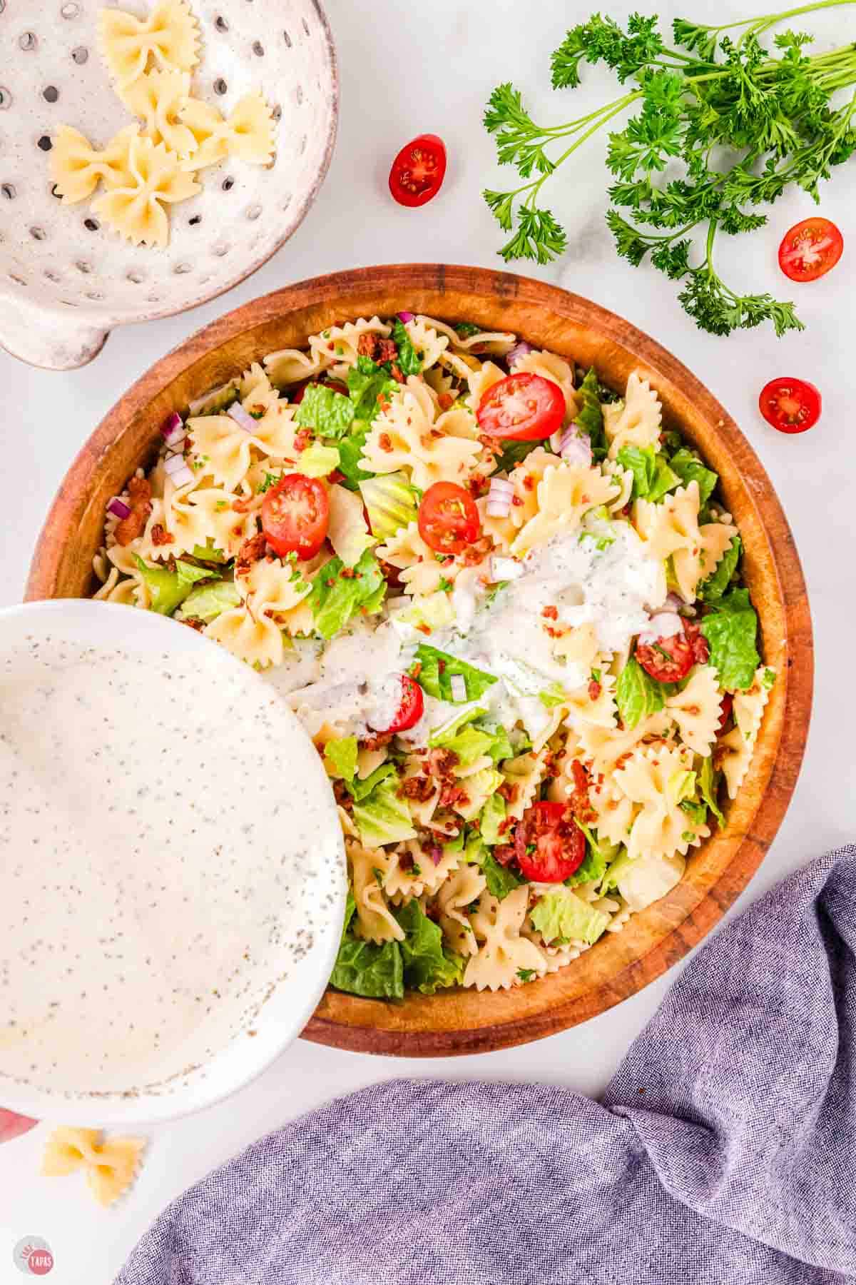 white bowl pouring a creamy dressing over a pasta salad