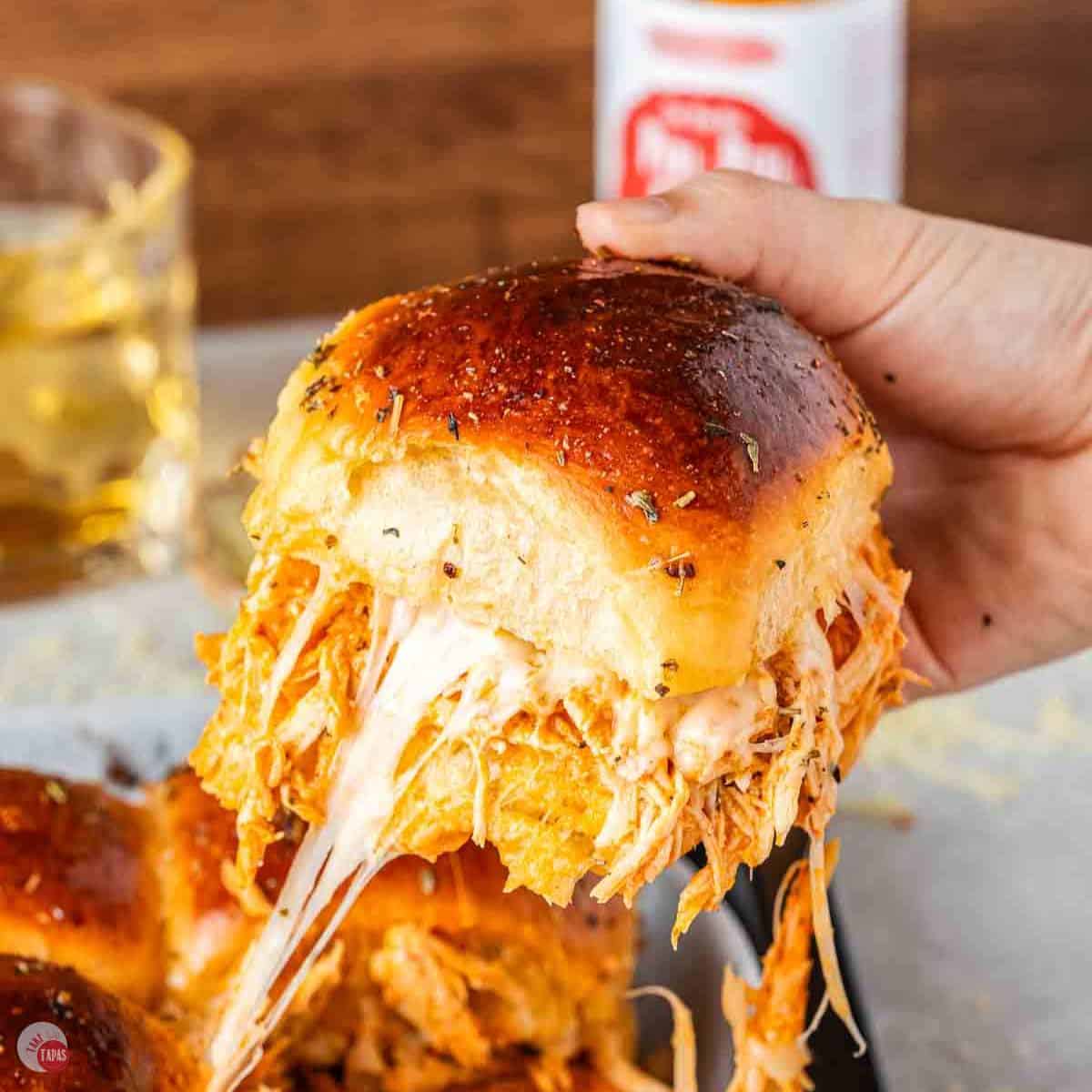 hand pulling a chicken slider out of a pan