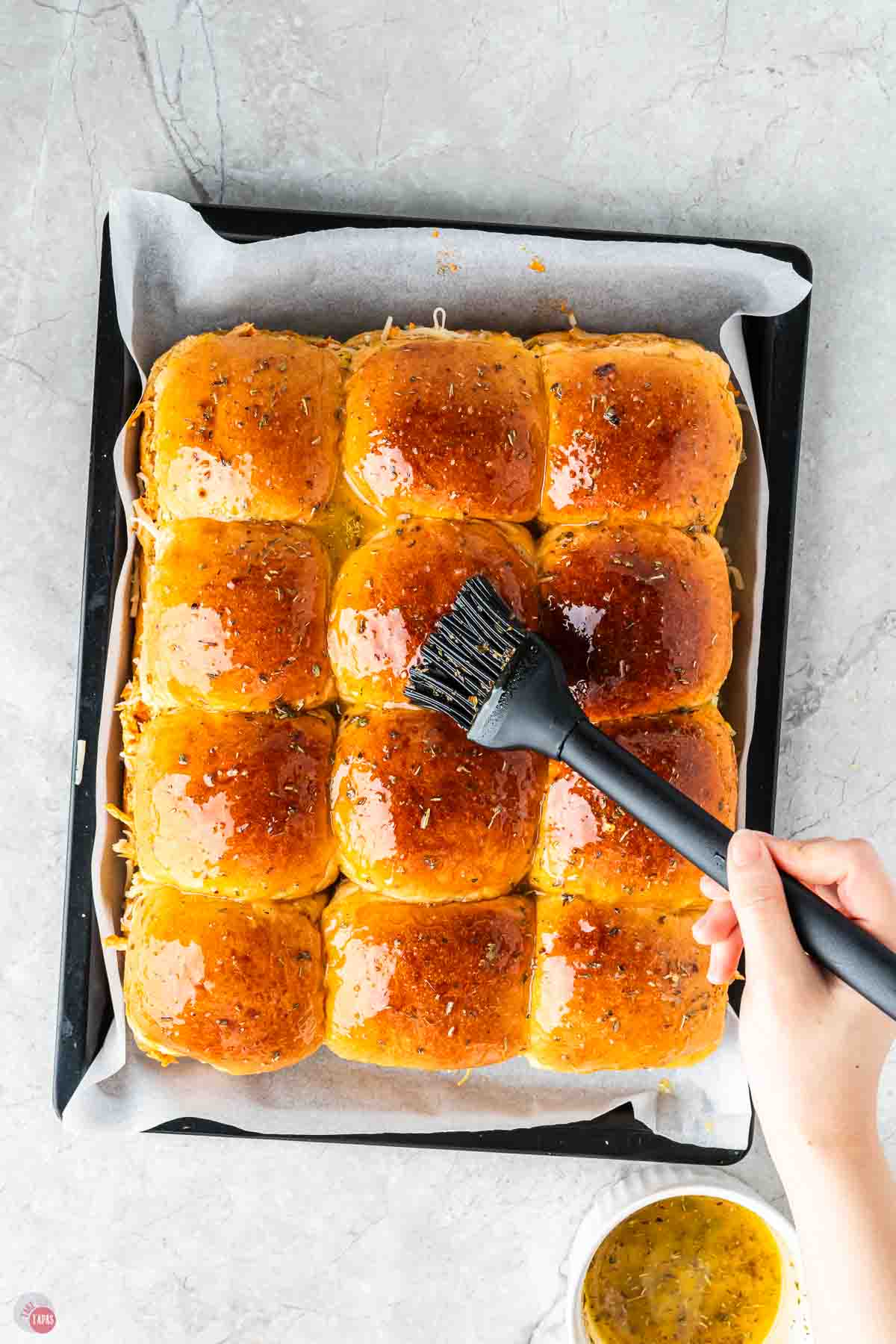 baking sheet with sliders being brushed with melted butter