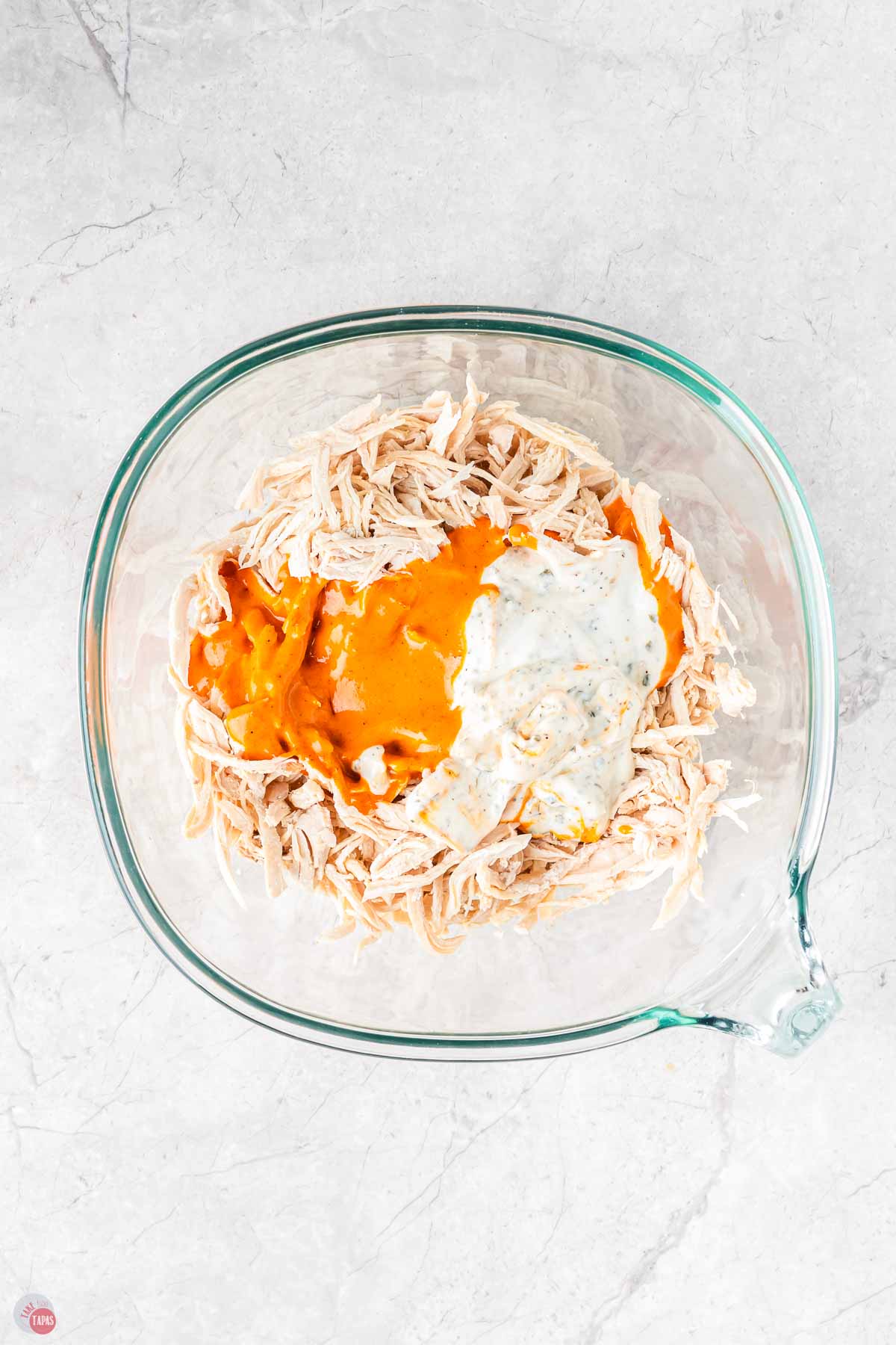 clear bowl of shredded chicken topped with buffalo sauce