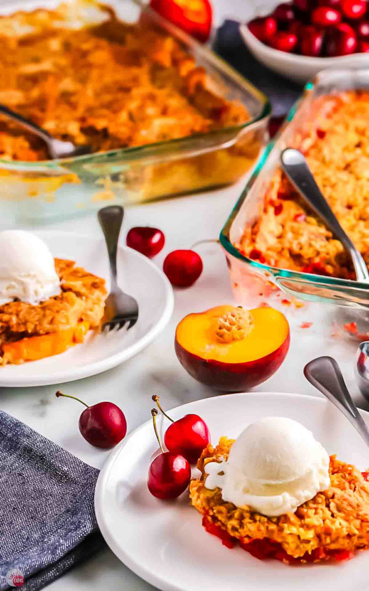 plate of cherry dump cake with fruit on the table behind it