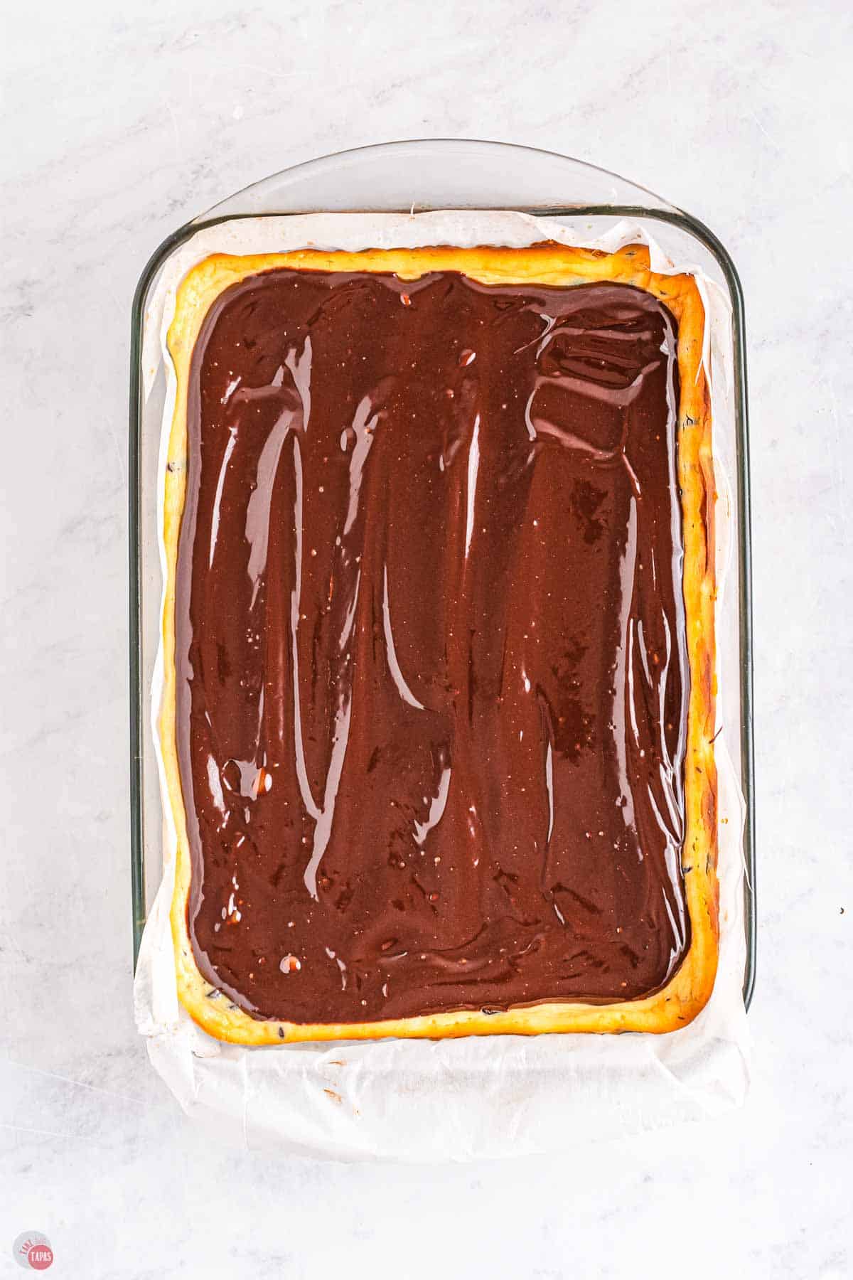 cheesecake in a baking dish with chocolate ganache spread over them