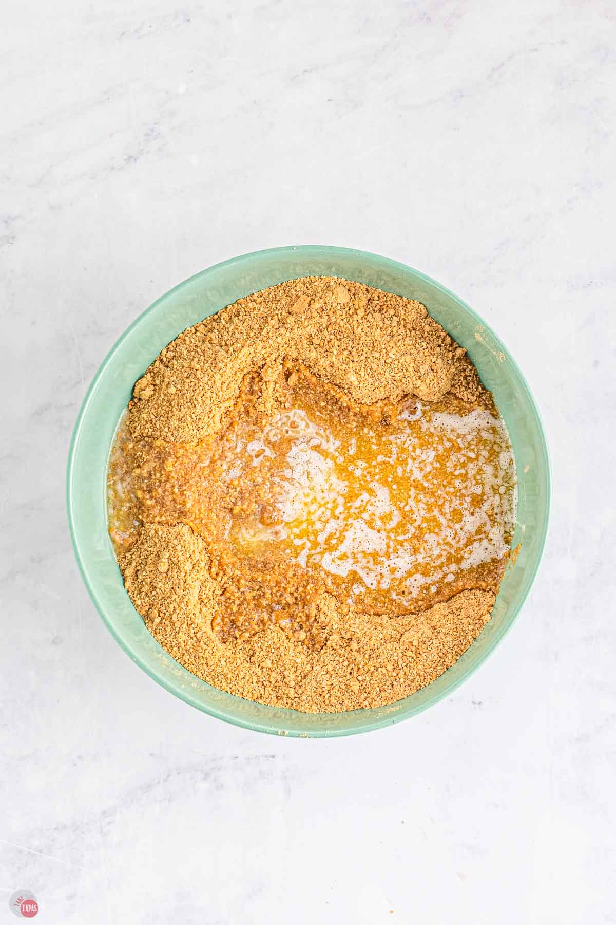 green bowl of graham cracker crumbs with melted butter