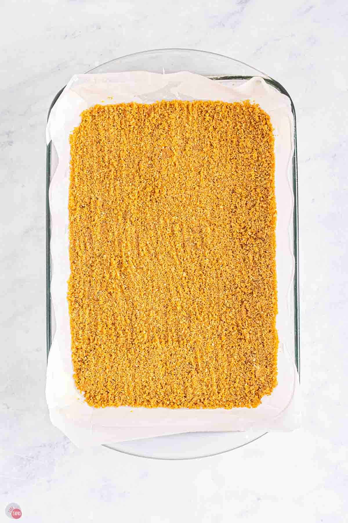 graham cracker crumbs pressed into a baking dish lined with parchment paper