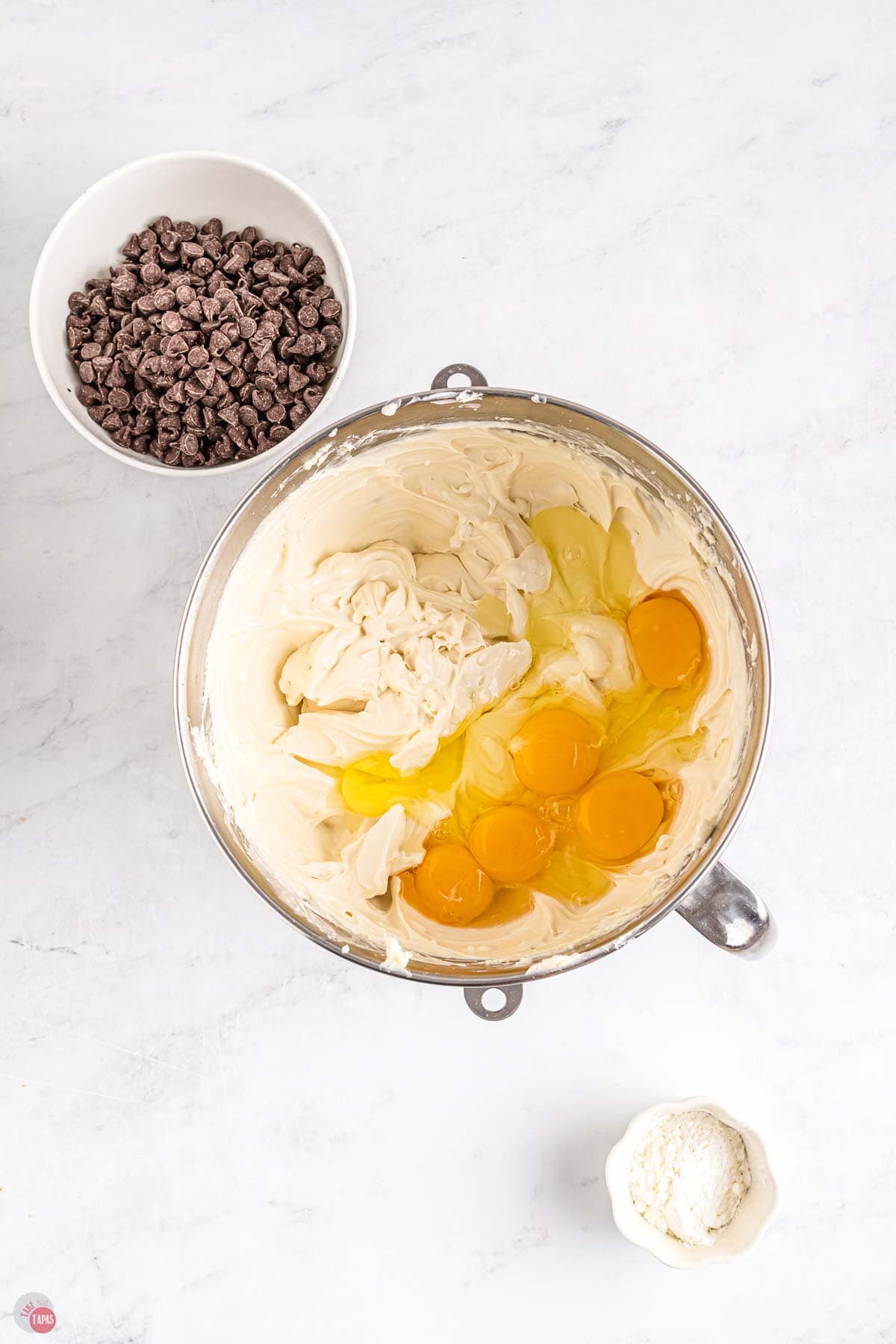 cheesecake mixture in a mixing bowl with eggs on top and a bowl of chocolate chips