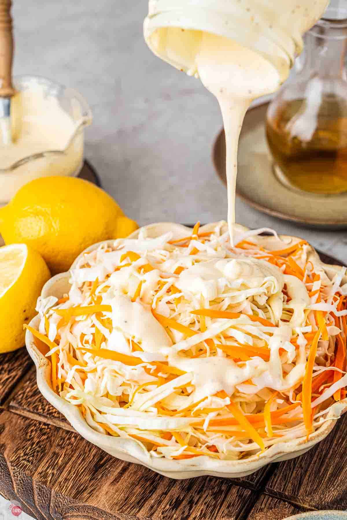 dressing being drizzled on a bowl of shredded cabbage