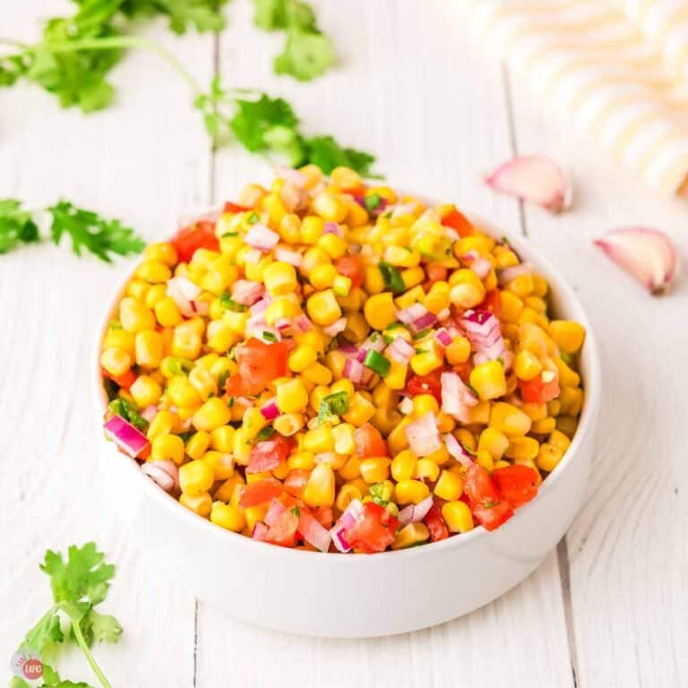 white bowl filled with corn salsa and surrounded by garlic cloves and cilantro
