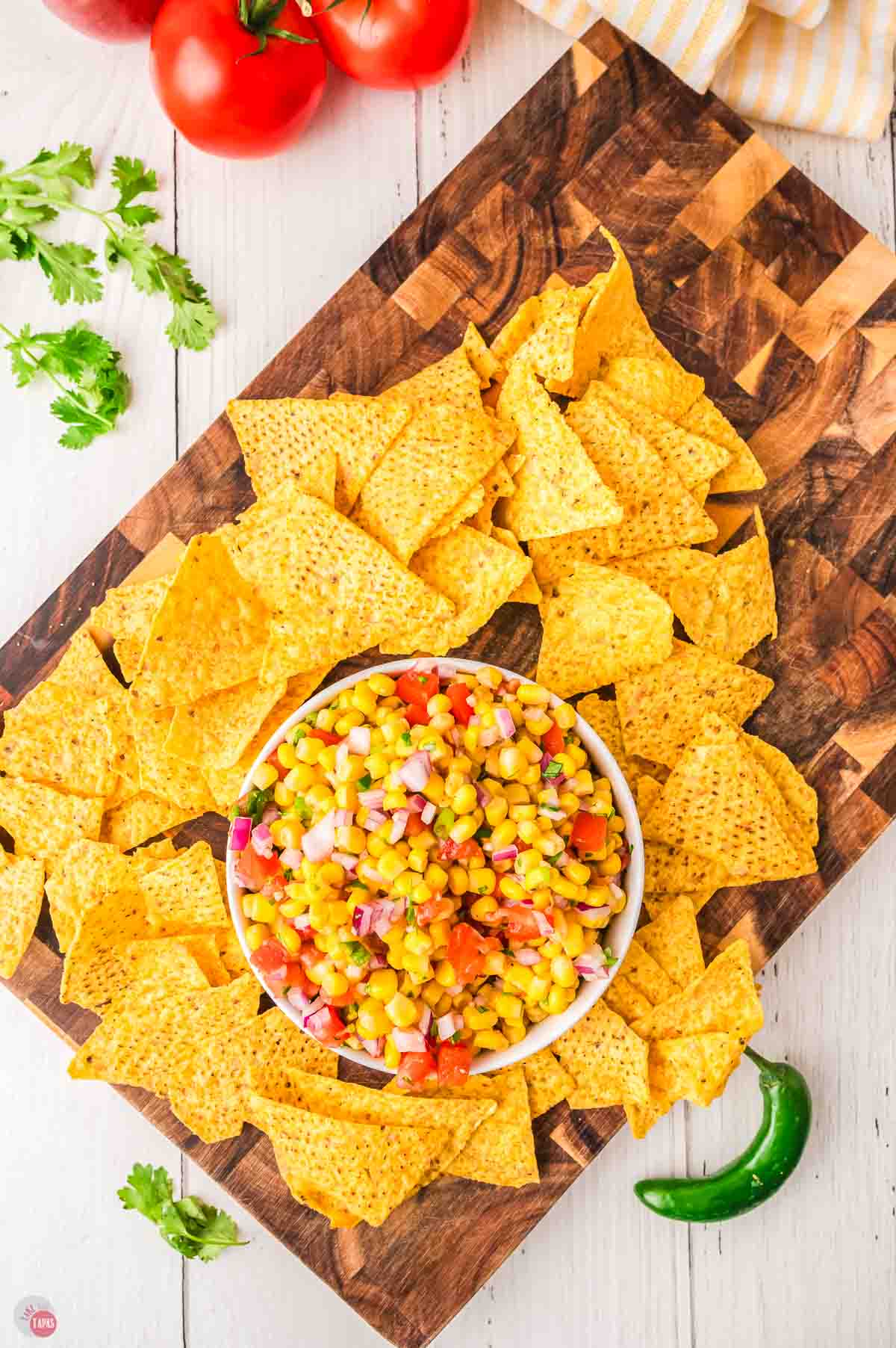 wood cutting board with a stack of tortilla chips and a bowl of salsa