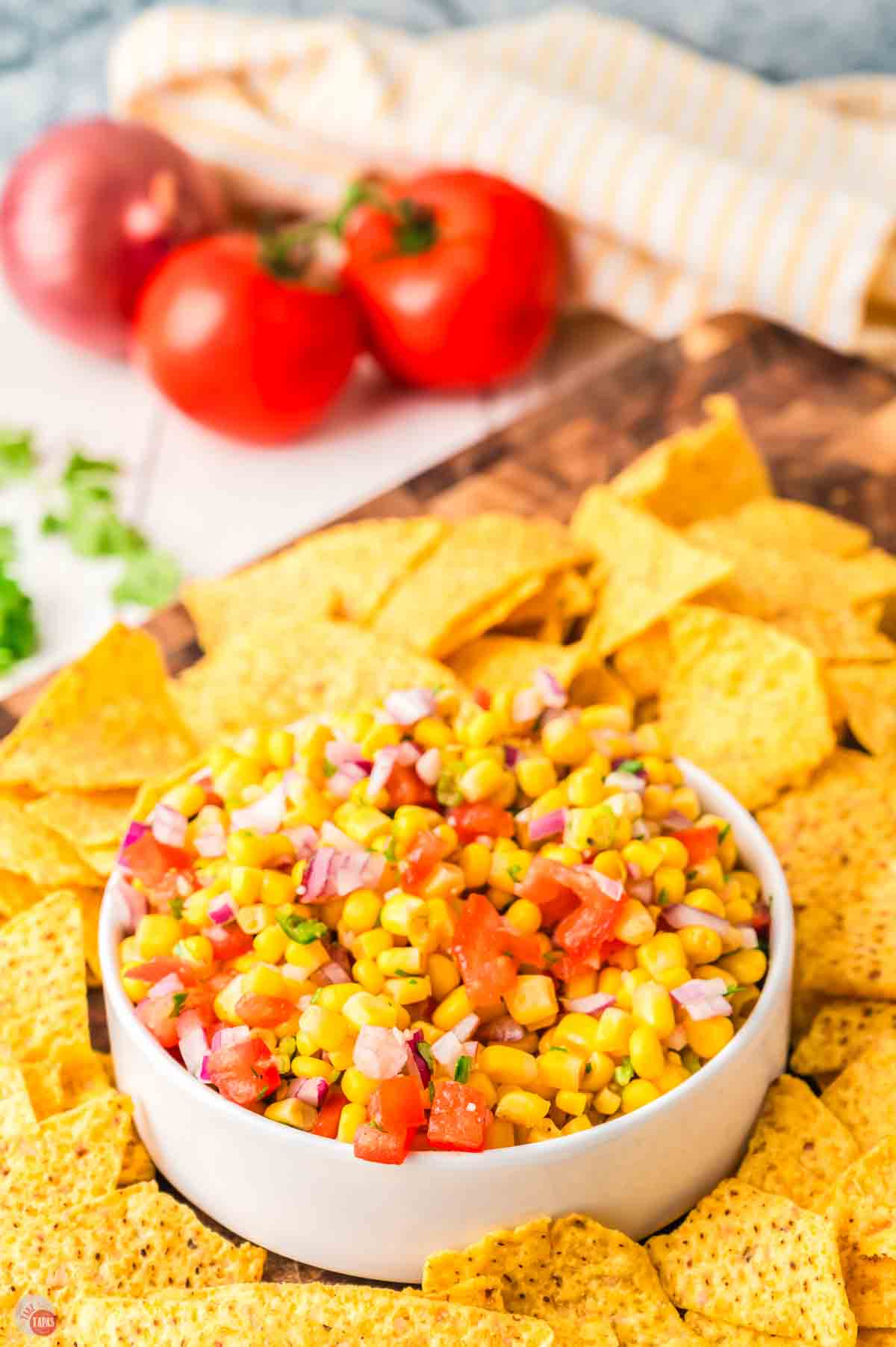 chip scooping salsa out of a bowl with a bunch of tomatoes in the back