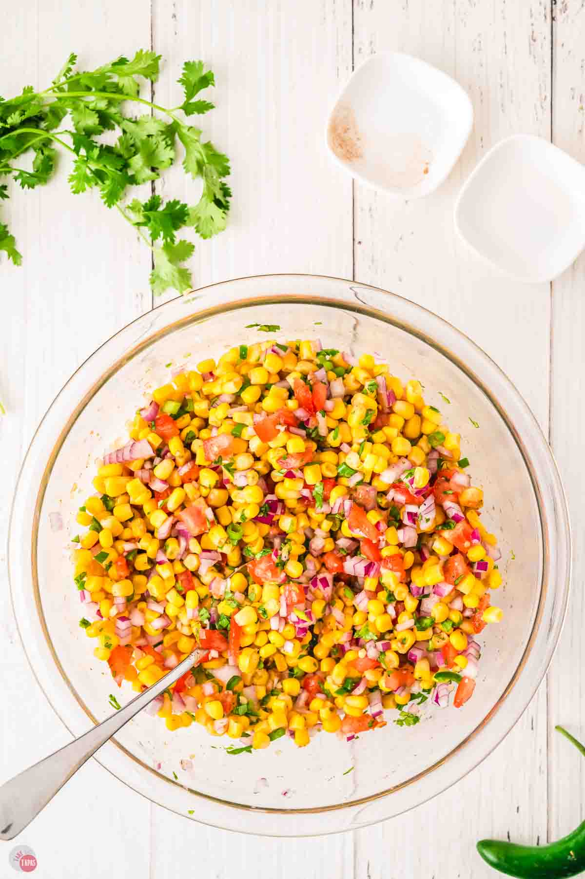 corn salsa in a clear mixing bowl with a spoon in it