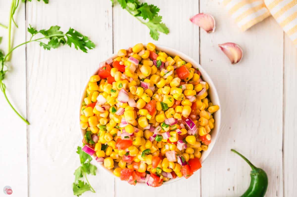 white bowl of corn salsa with garlic cloves around it