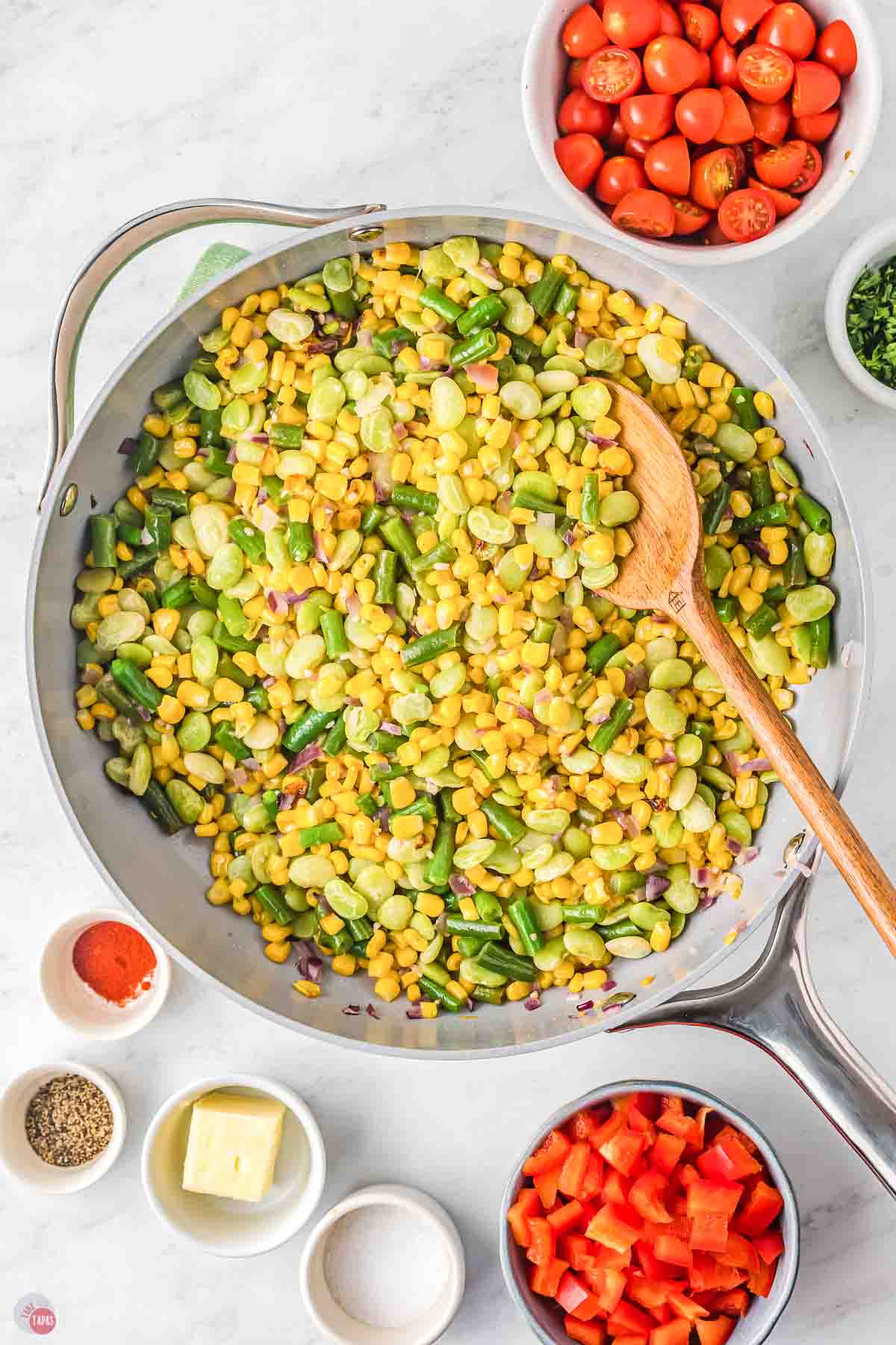 corn, lime beans, and green beans in a skillet being stirred with a wood spoon