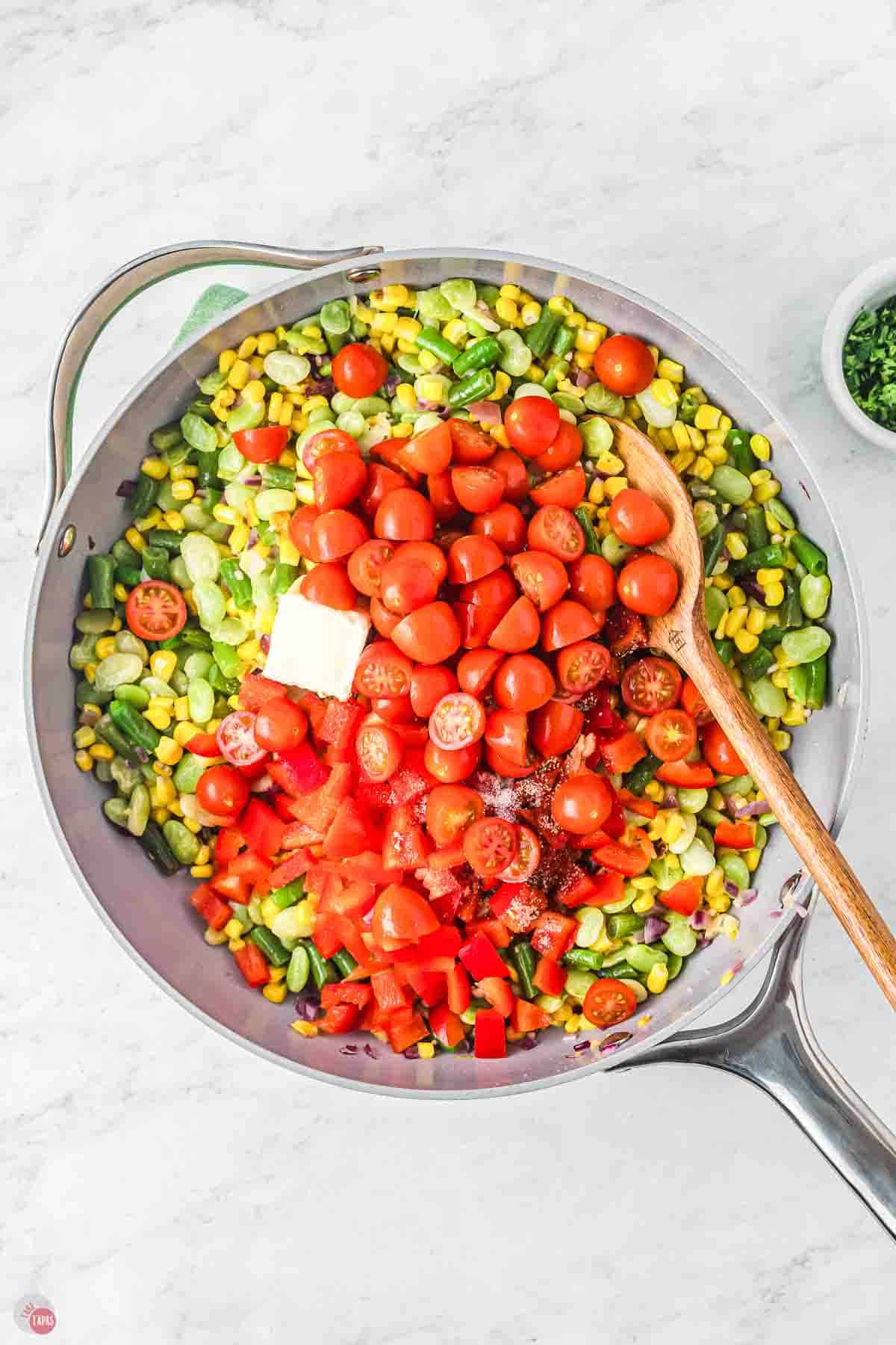 skillet with vegetables and tomatoes being stirred in