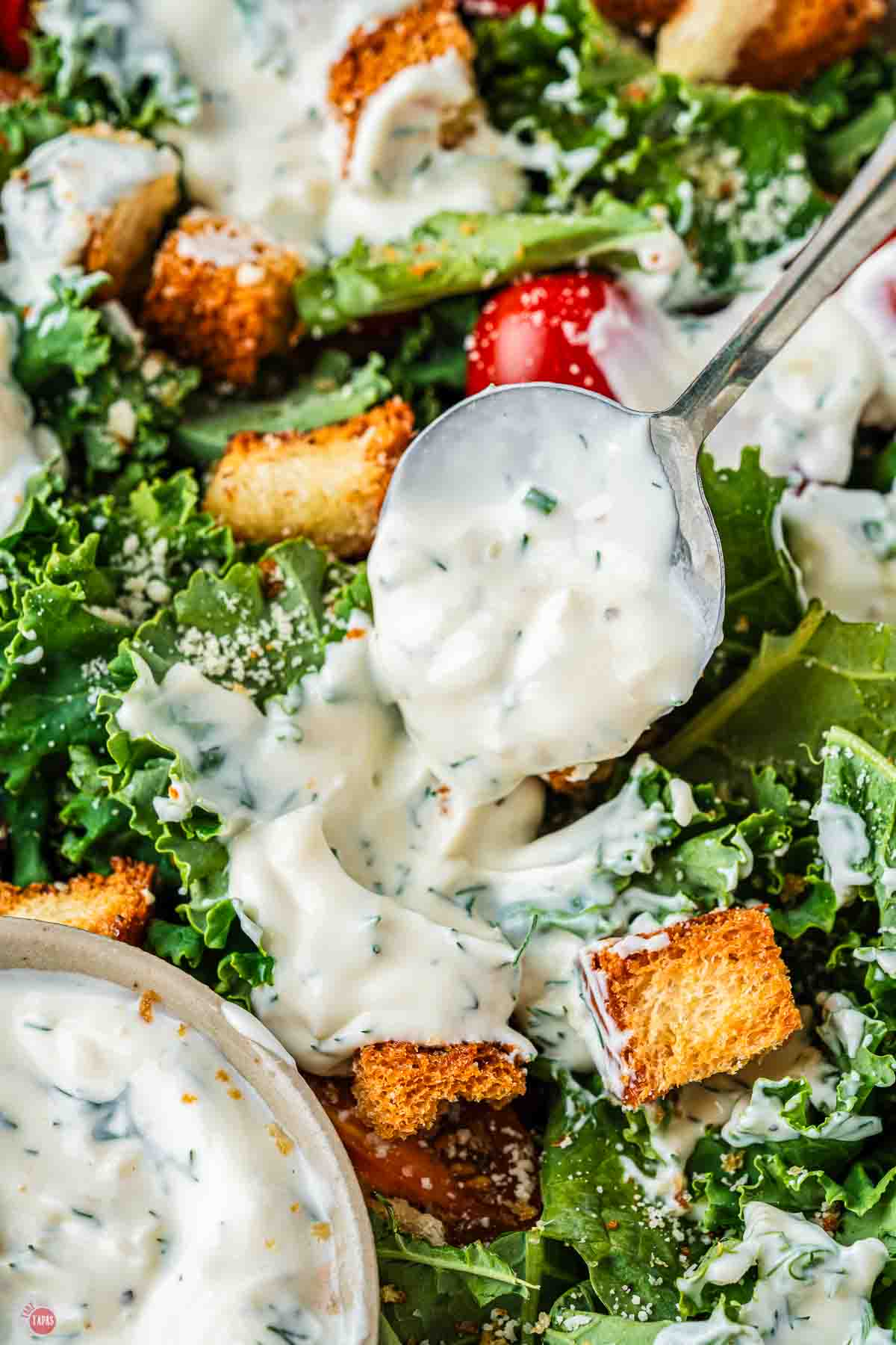 spoon pouring salad dressing on mixed greens
