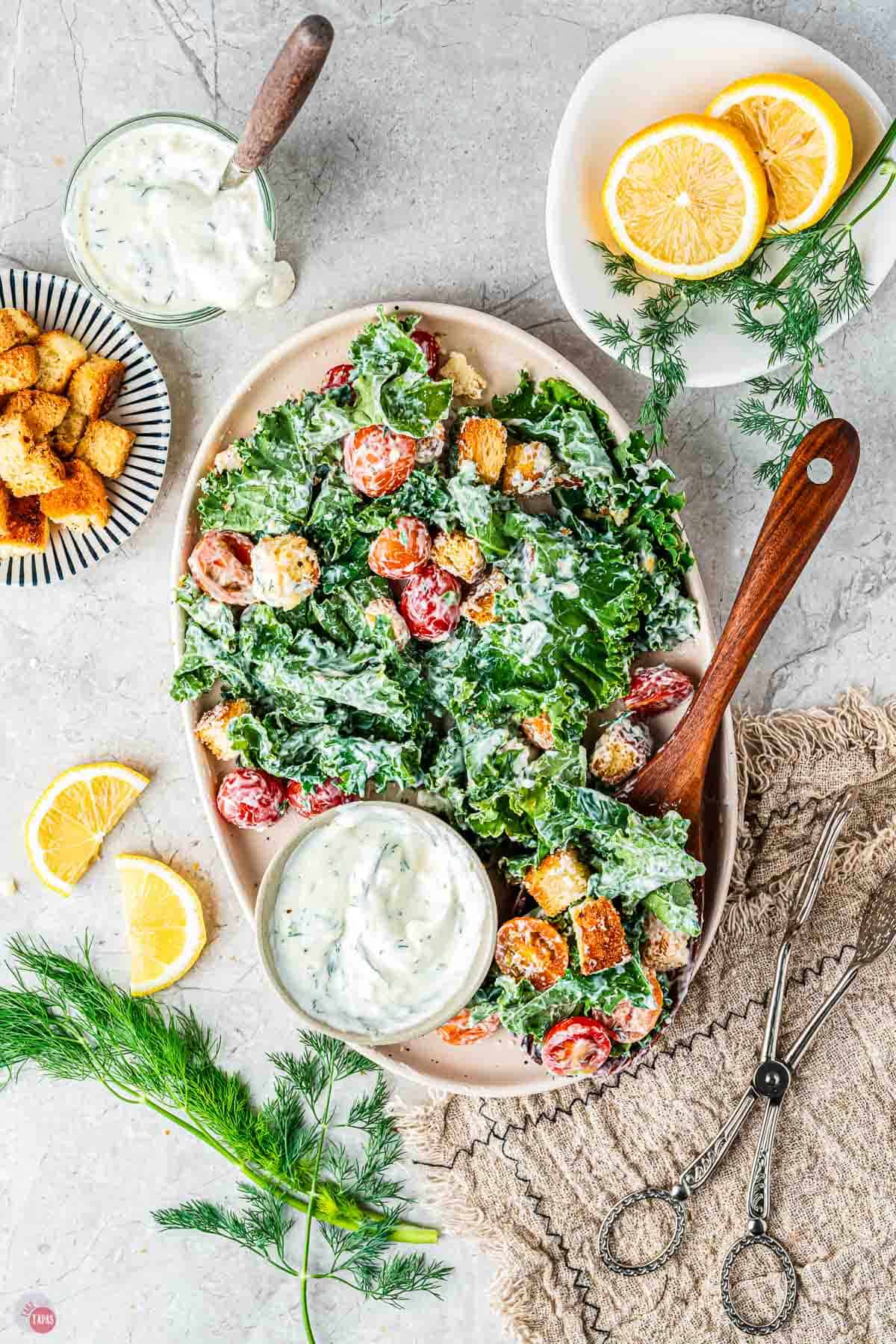 platter of salad with wood spoon and a small bowl of croutons