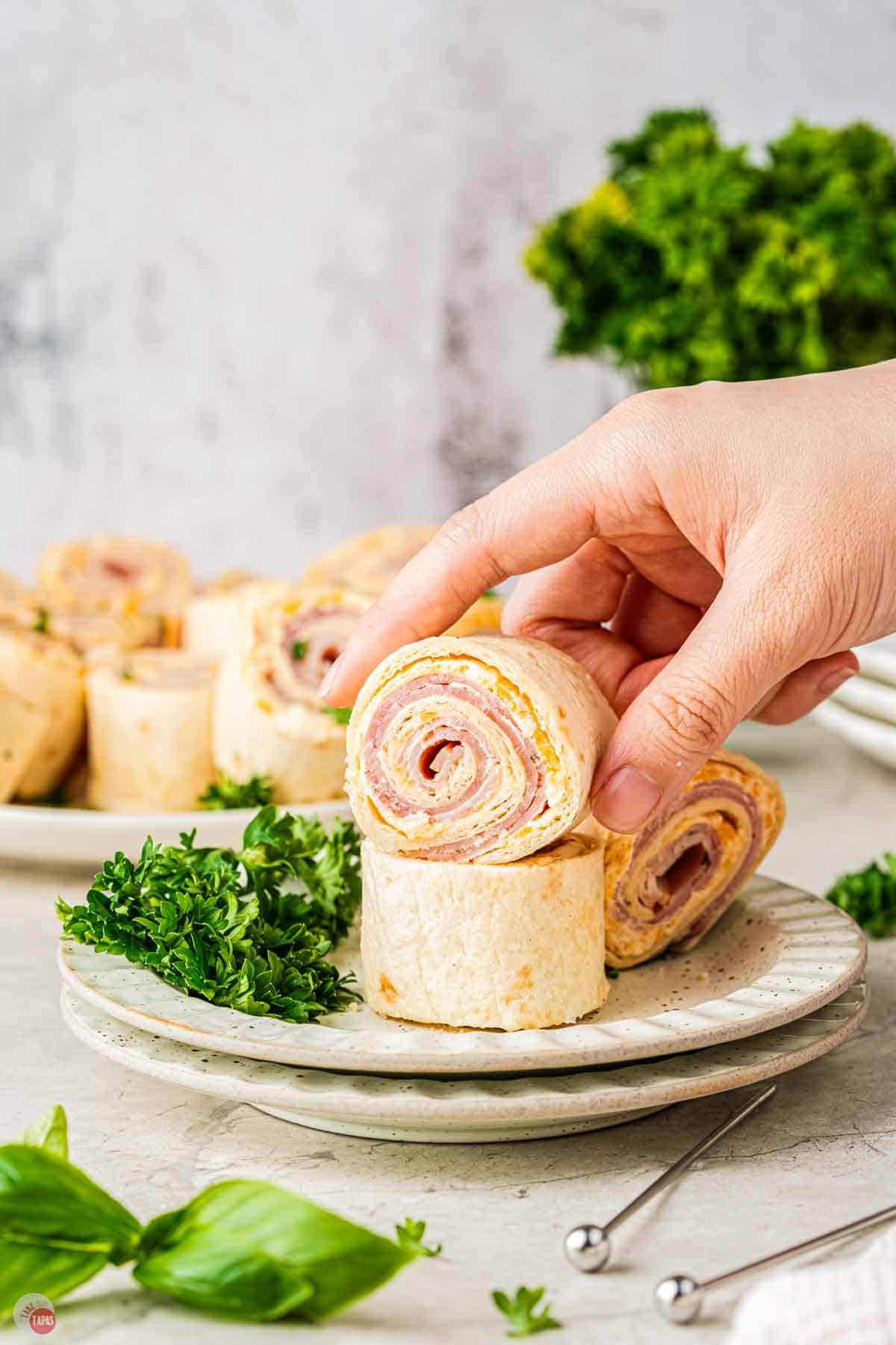 hand picking up a ham and cheese roll up sandwich off a plate