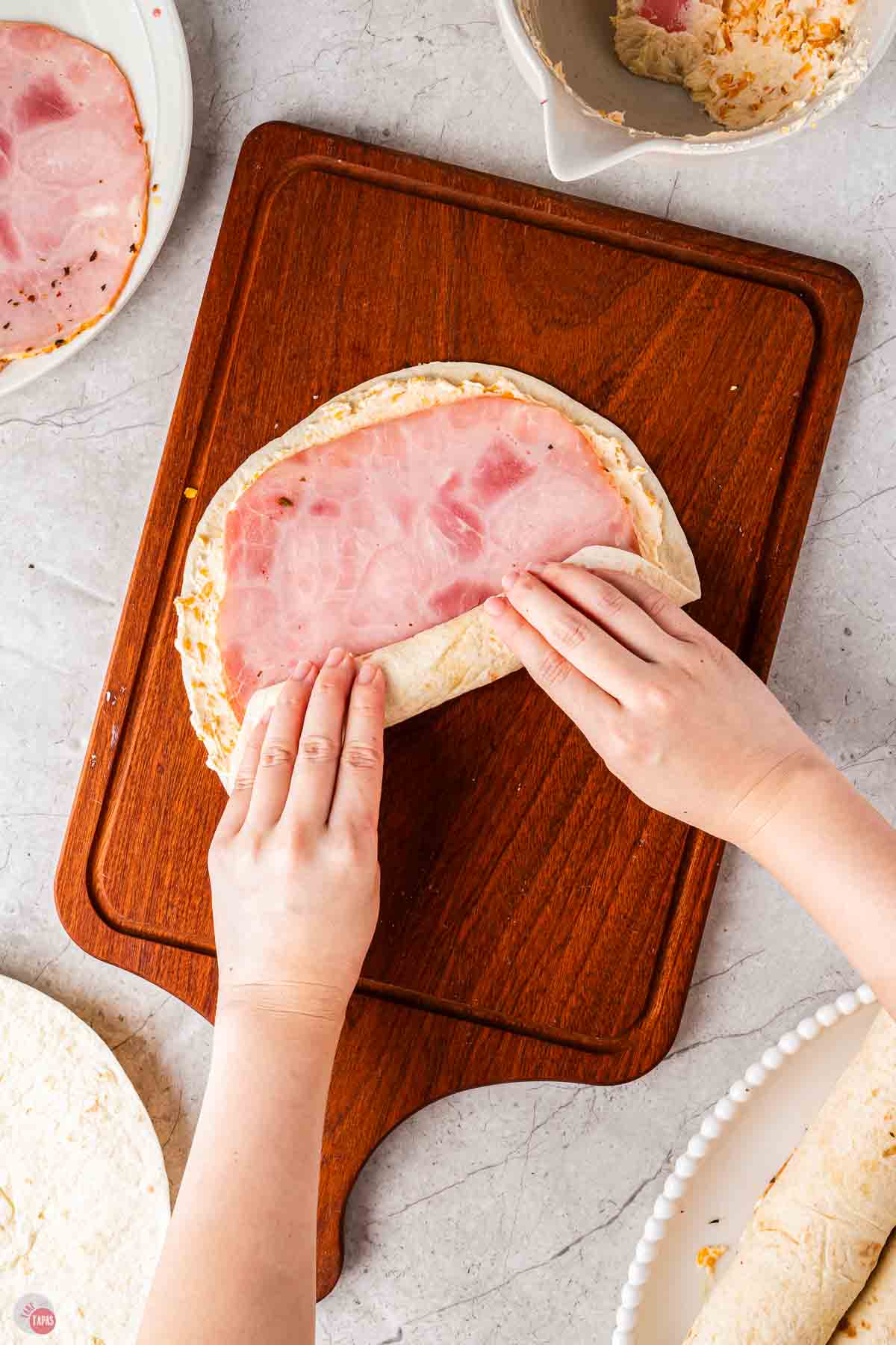 hand rolling up a tortilla stuffed with sliced ham