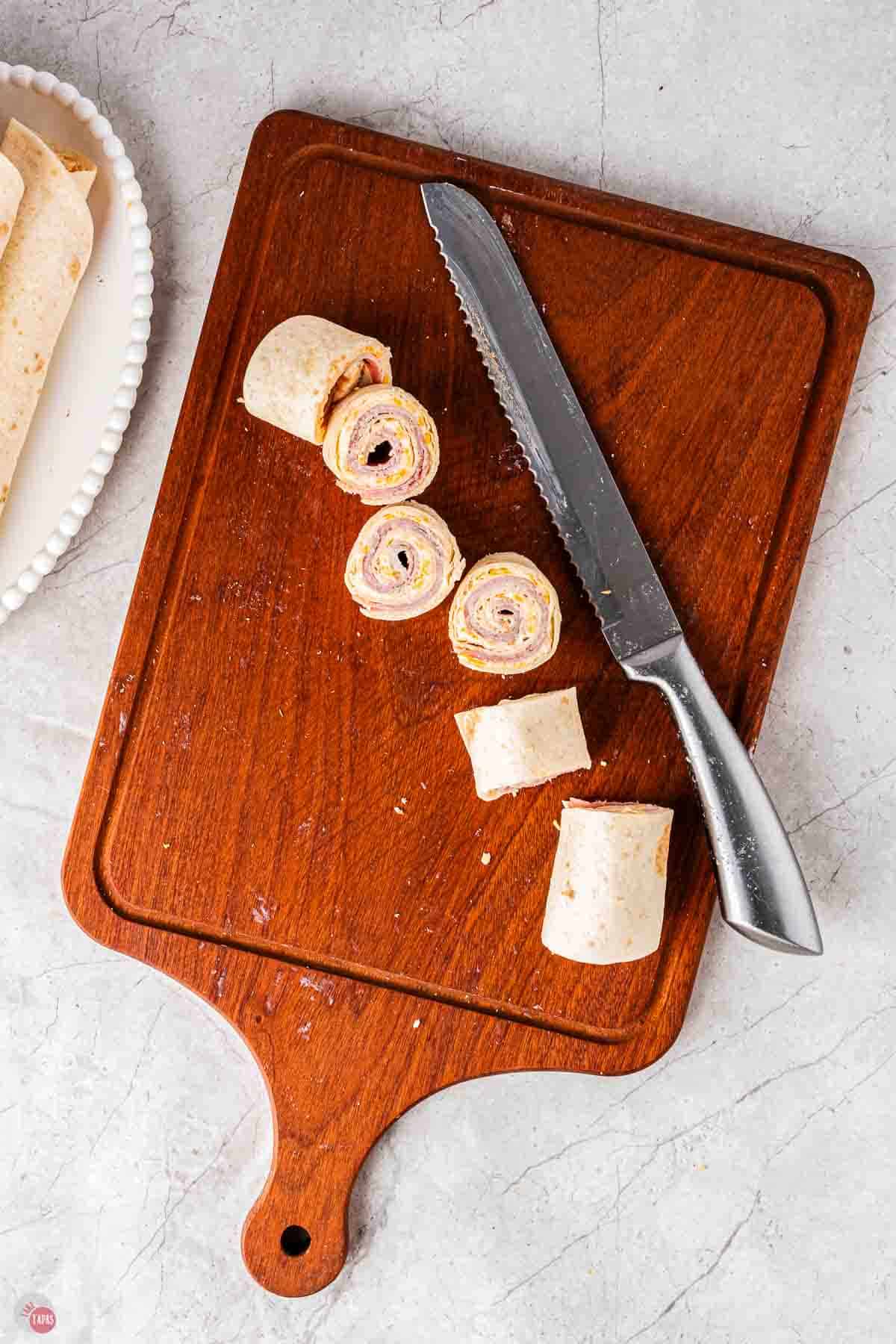 cutting board with knife slicing a rolled up tortilla