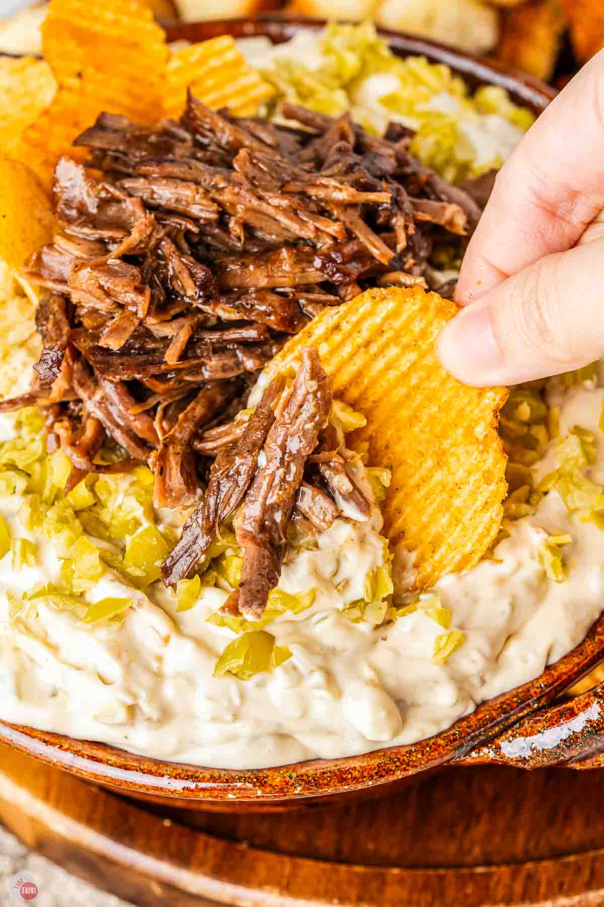 hand with potato chip scooping dip out of a bowl