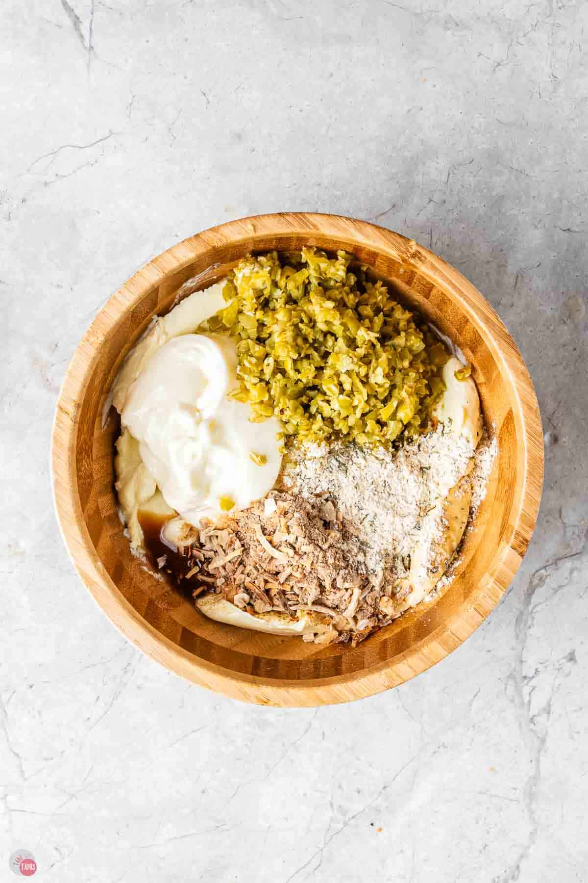wood bowl with sour cream, spices, and chopped vegetables in it