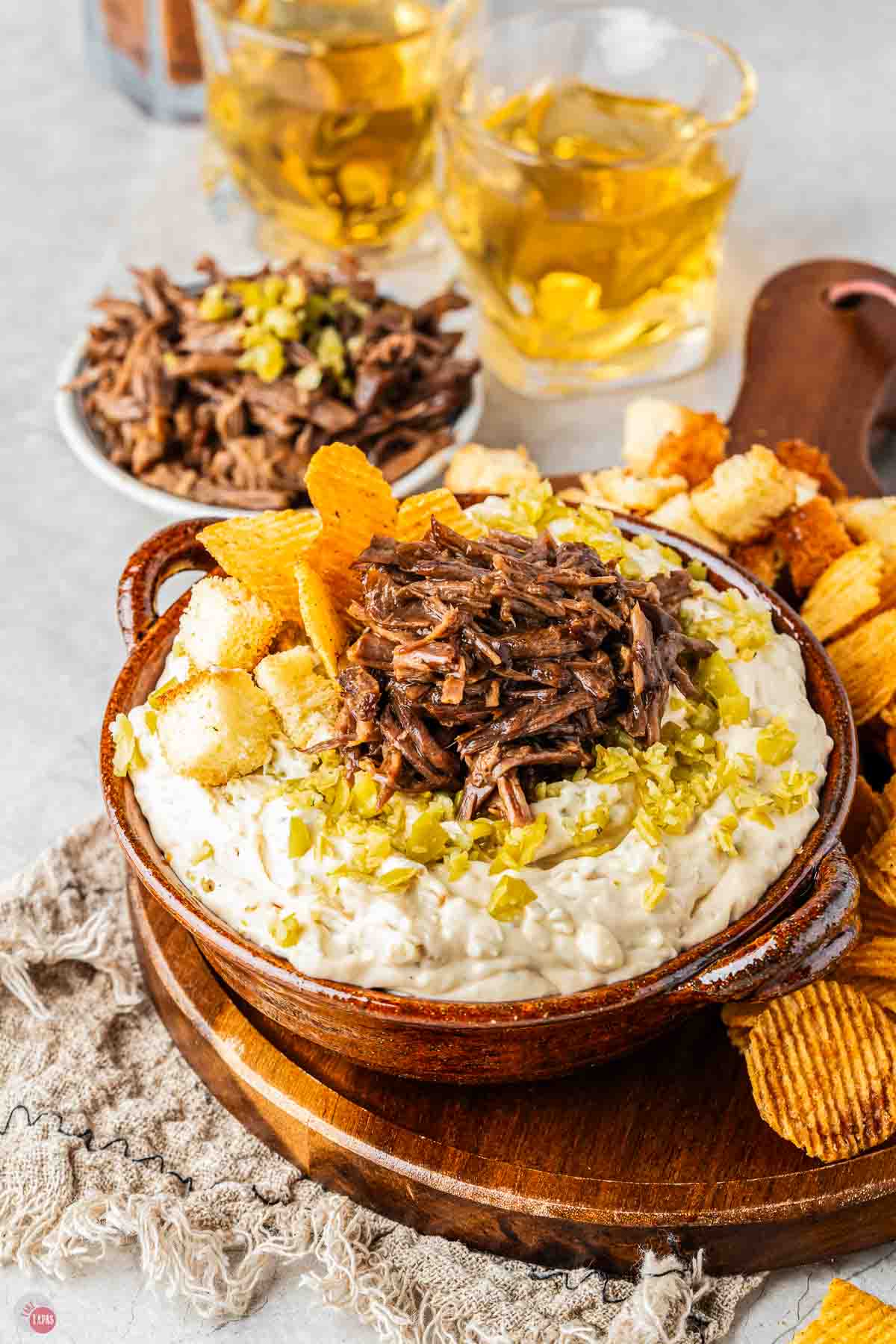 wood bowl of dip topped with meat and surrounded by crackers
