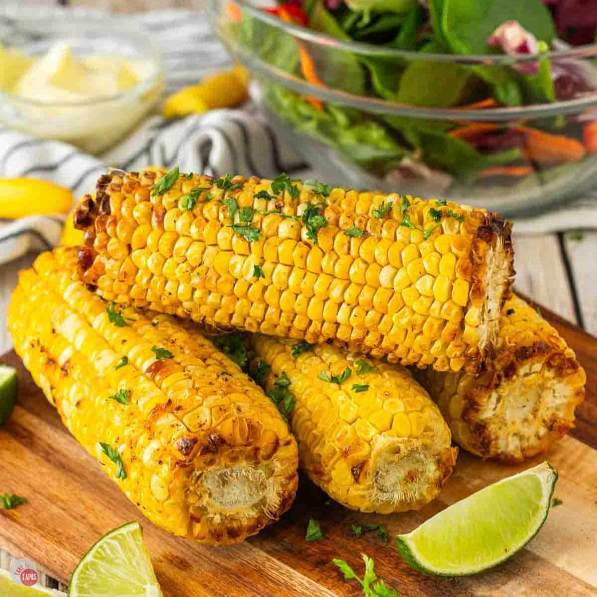 stack of roasted corn on a cutting board with lime wedges