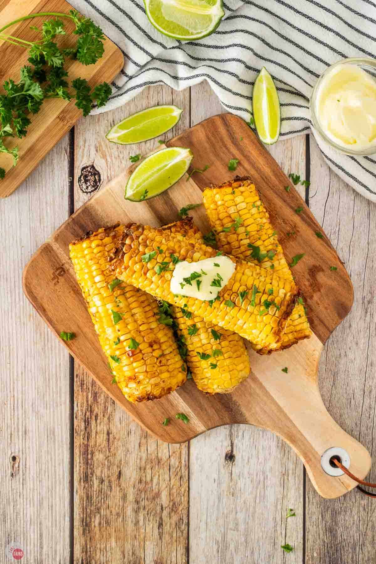stack of roasted corn on a cutting board with fresh parsley and butter