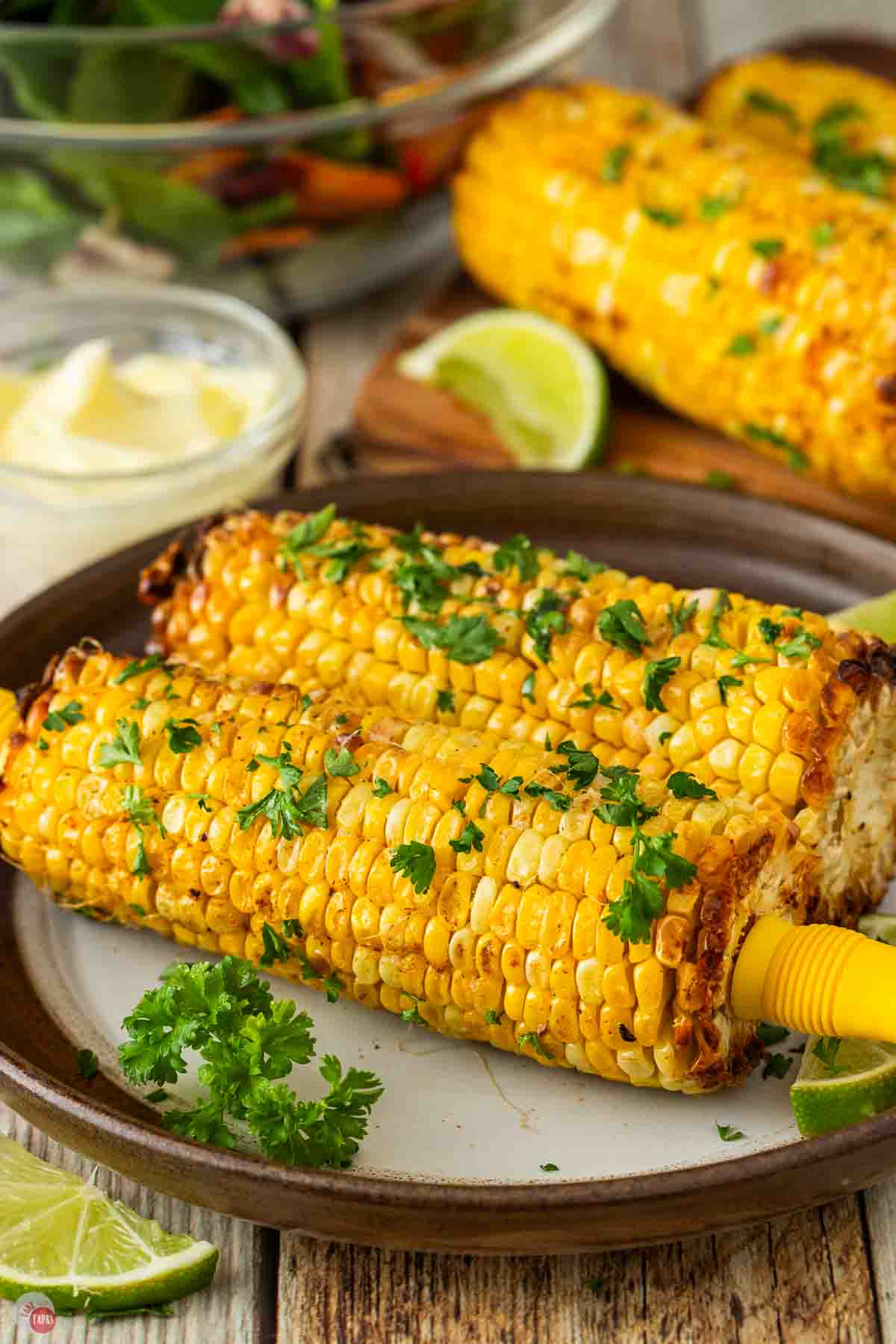 two cobs of corn with handles in the ends on a plate with parsley sprinkled on top