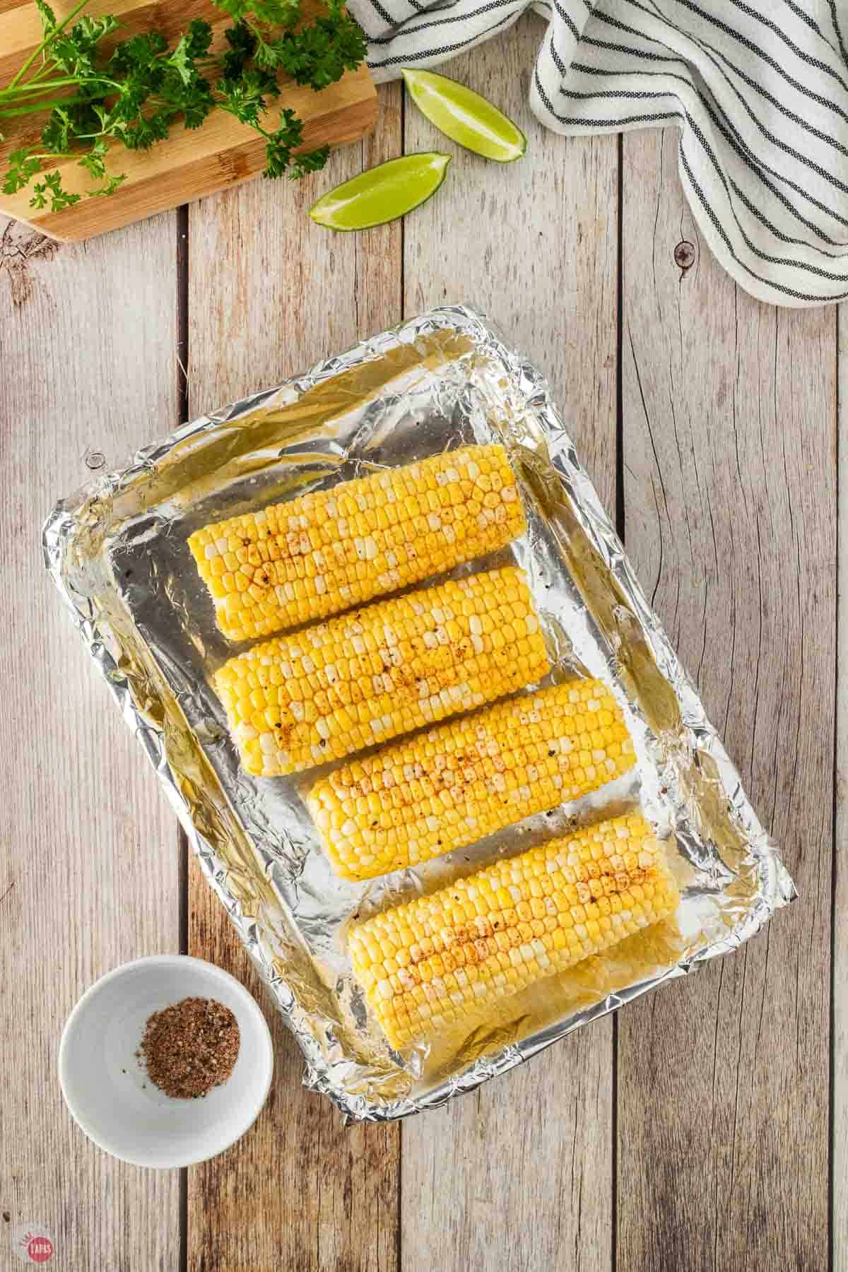corn cobs on a foil lined baking sheet with spices on them