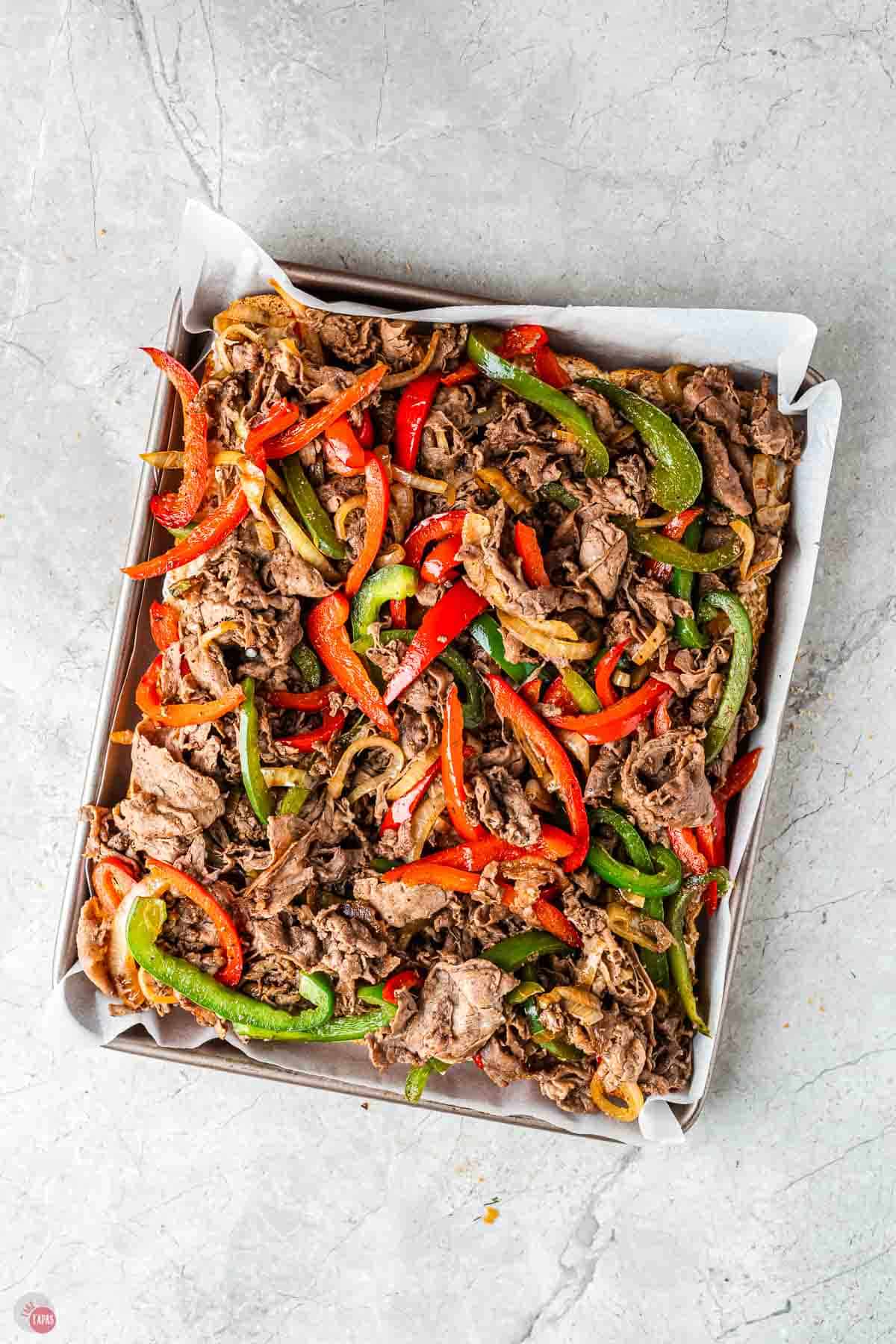 slider buns on a baking sheet topped with shredded steak and peppers